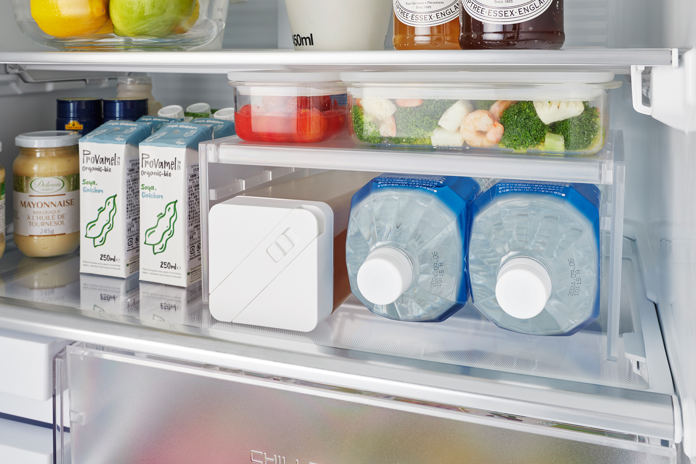 White Expandable Refrigerator Riser Shelf by Yamazaki Home is visible in a refrigerator storing various food items, maximizing space efficiently.