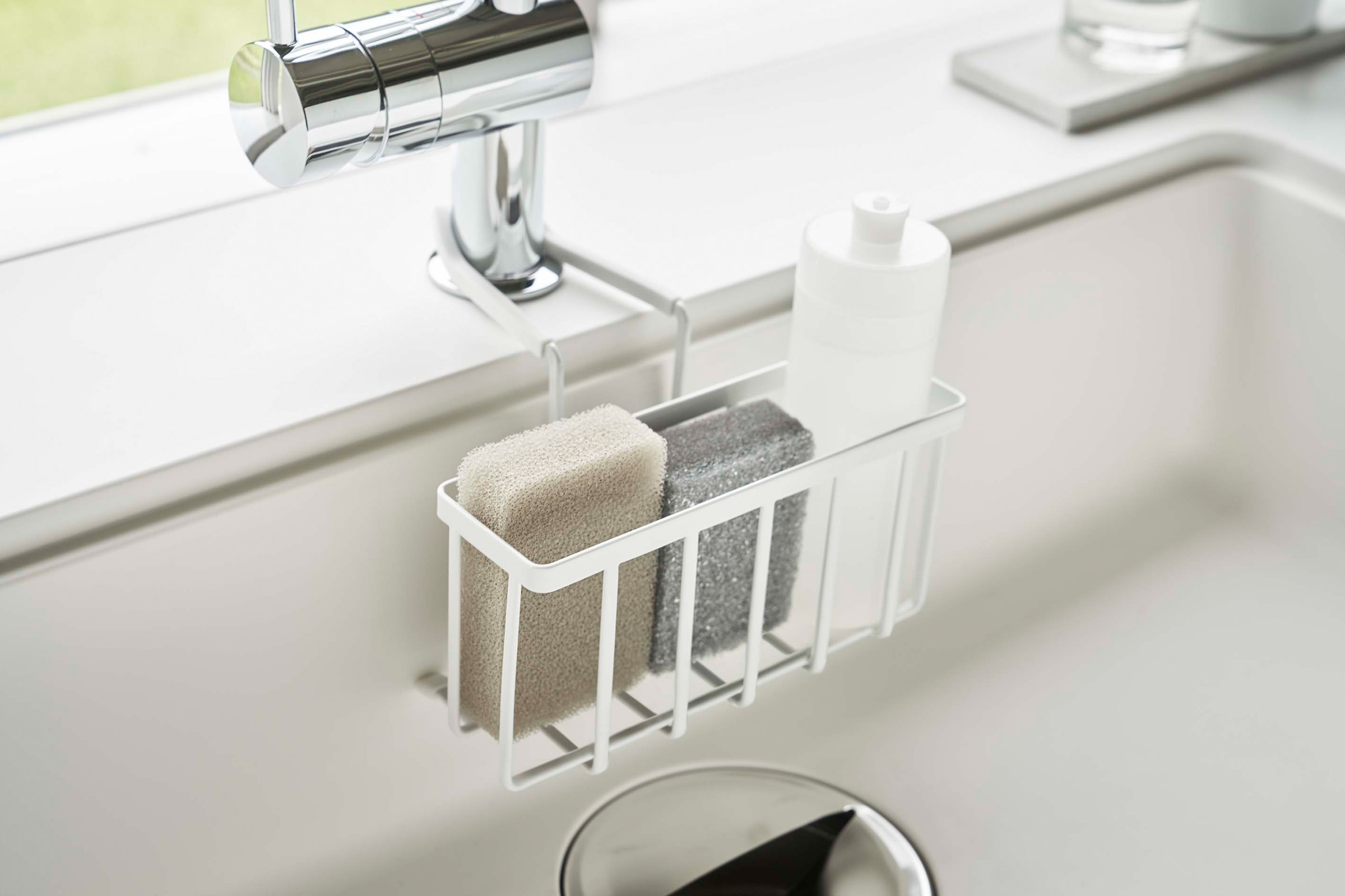 Close up side view of Yamazaki Home white Faucet-Hanging Sponge Caddy in a sink