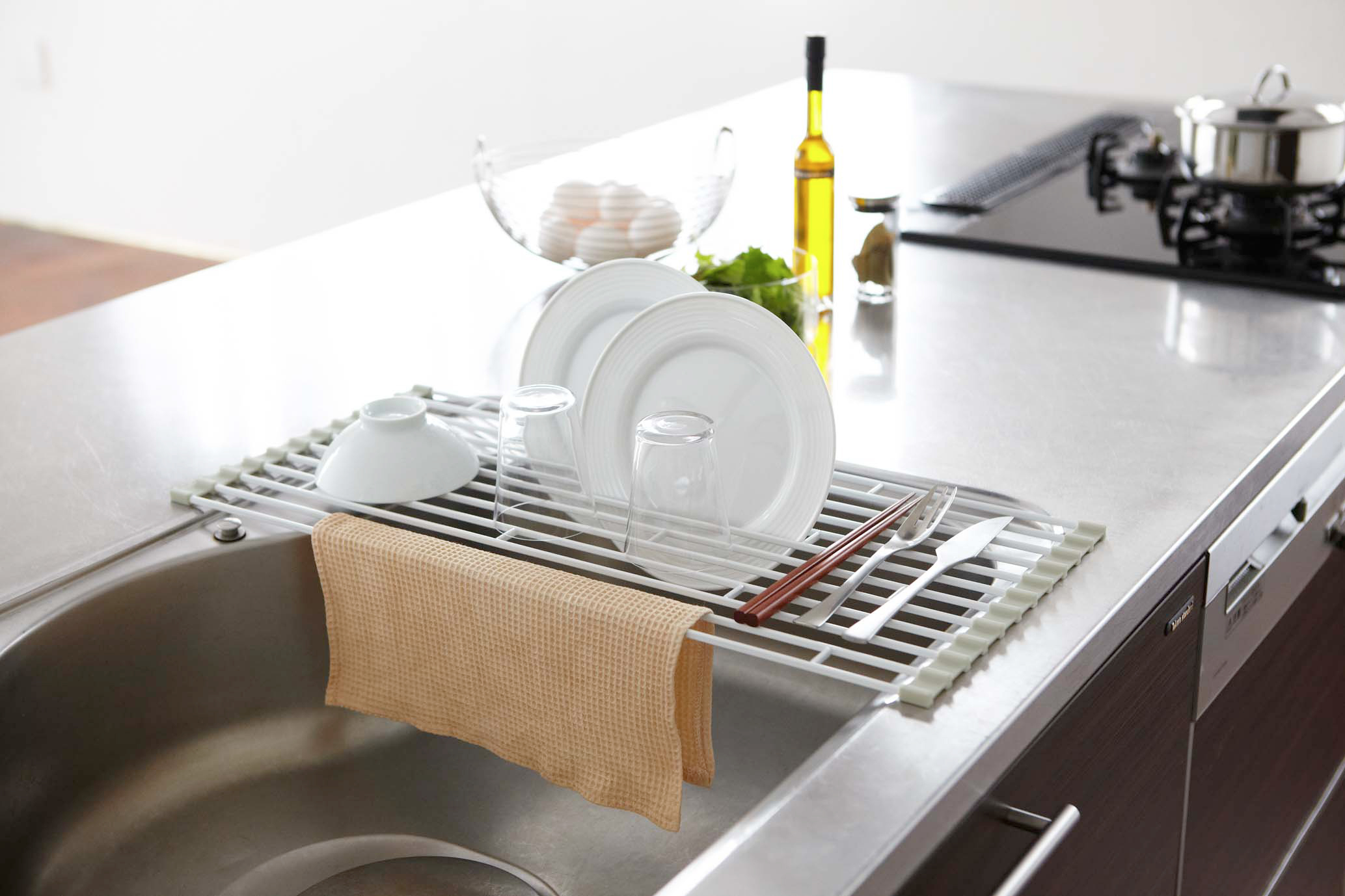 Yamazaki Home Over-the-Sink Dish Drainer holding dishes, cups, bowl, utensils, and dish rag over kitchen sink.