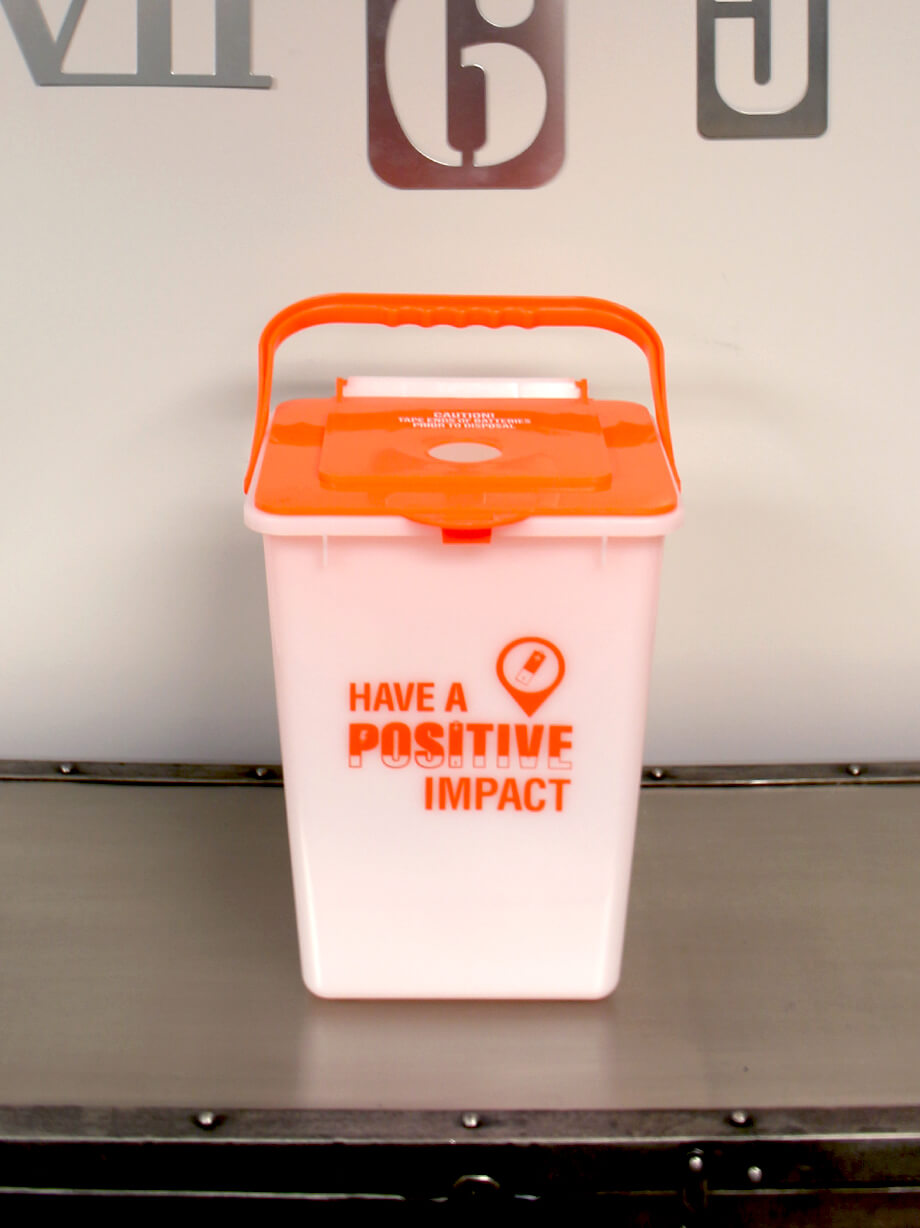 orange and white used battery bin for collecting batteries for recycling sitting on a cabinet in a corporate office area