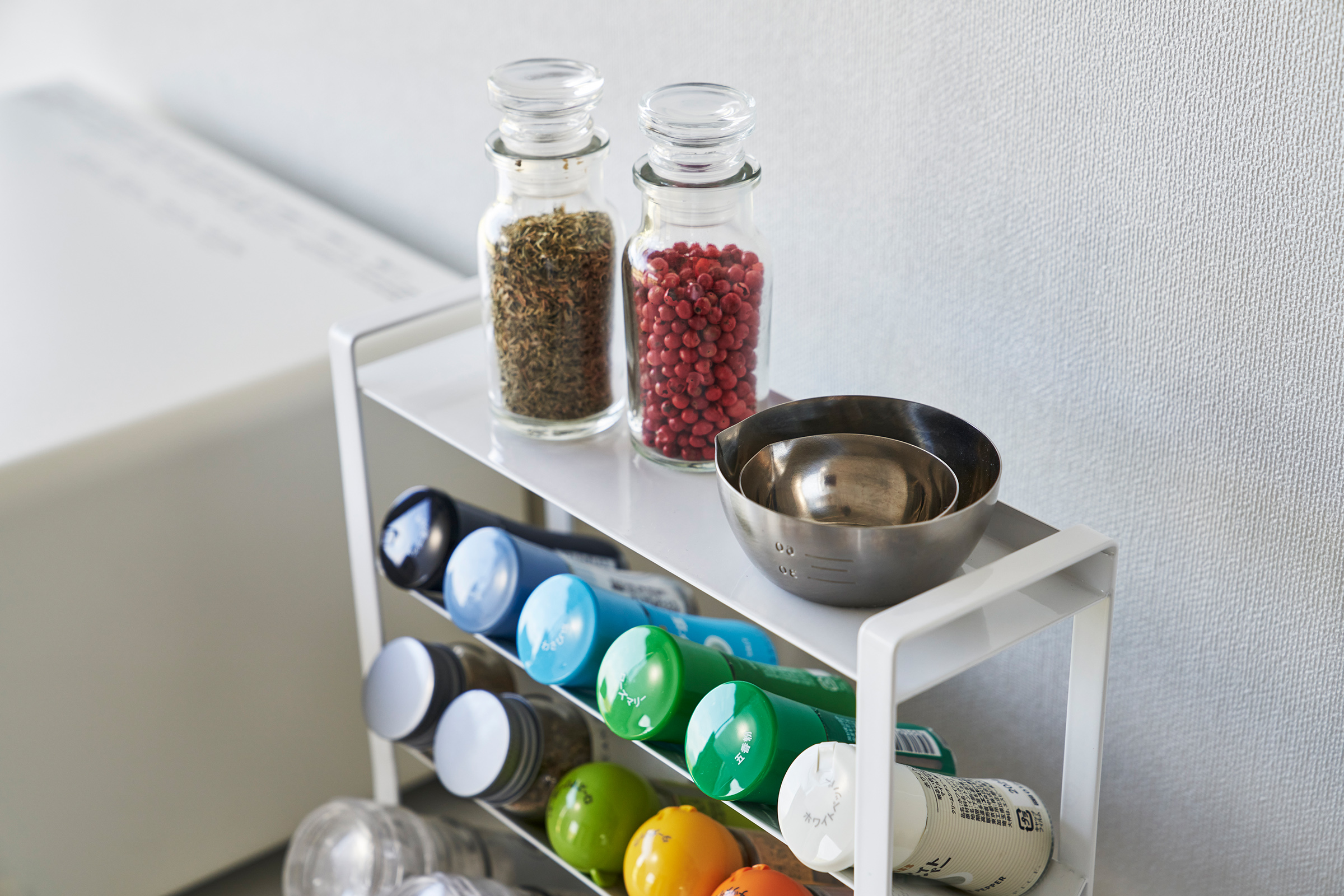 Close-up of a White Four-Tier Slim Spice Rack by Yamazaki Home with spices, oils, and cooking utensils on a kitchen counter.