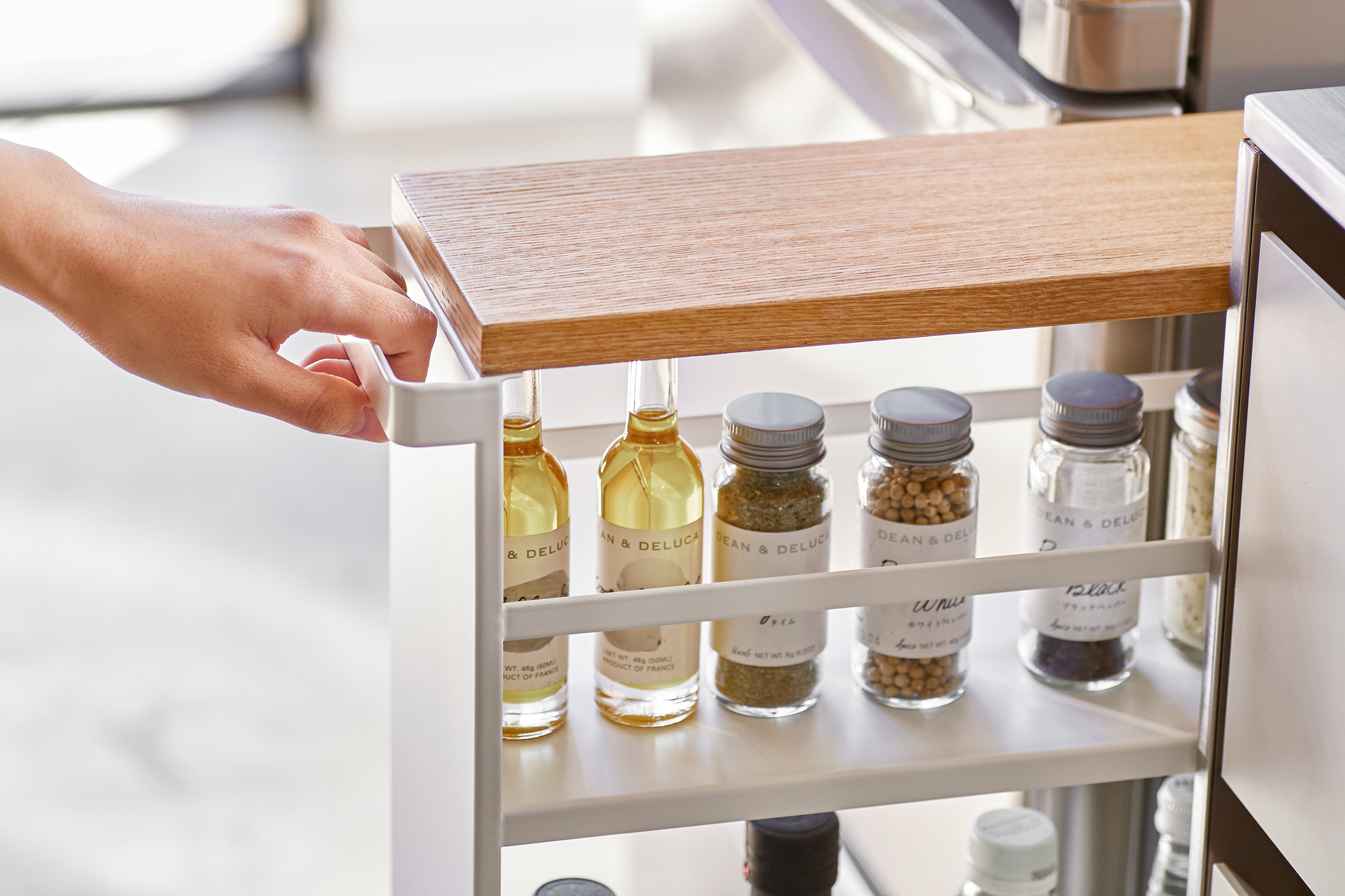 Close up front view of Yamazaki Home white Rolling Storage Cart held by handle and holding spices and ingredients in kitchen.