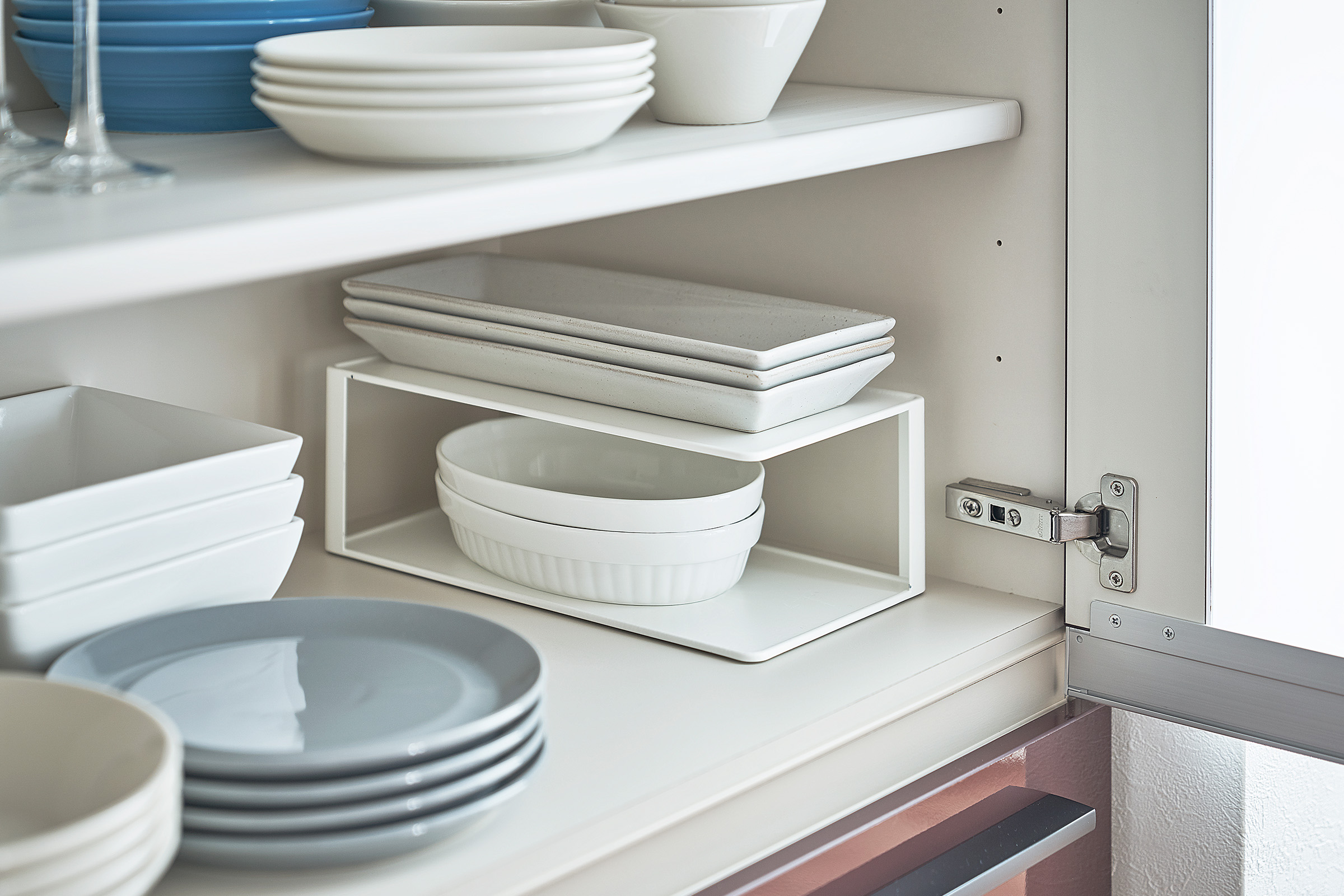 Two-Tier Cabinet Organizer by Yamazaki Home in white in a cabinet holding stacks of small plates.
