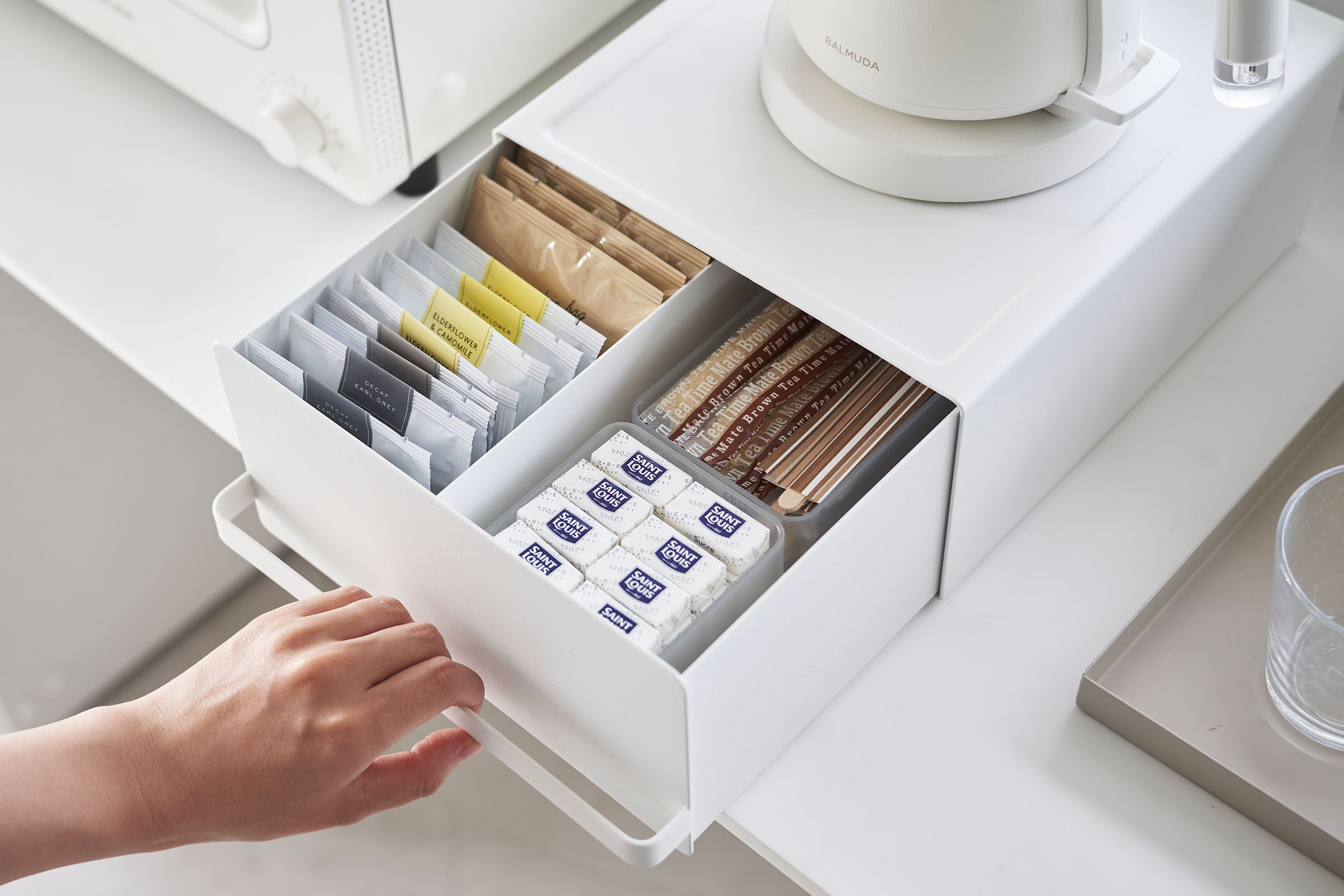 Someone is holding a handle of Yamazaki Home White Countertop Rack with Drawer holding tea bags.