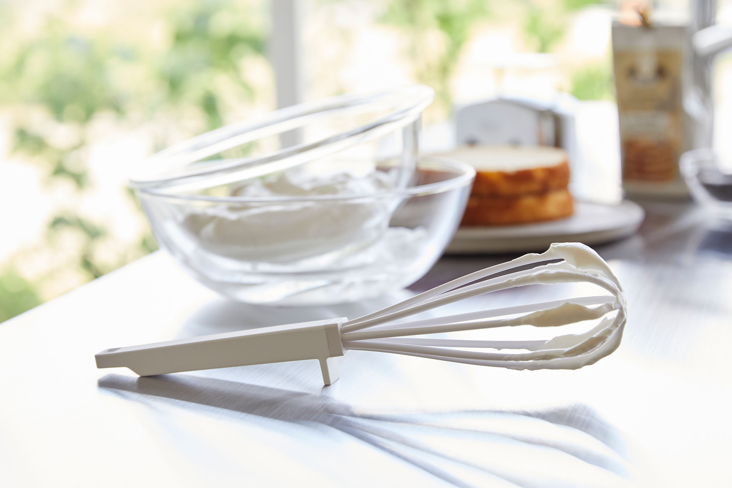 A white Yamazaki Floating whisk with meringue on it resting on a table next to two bowls.