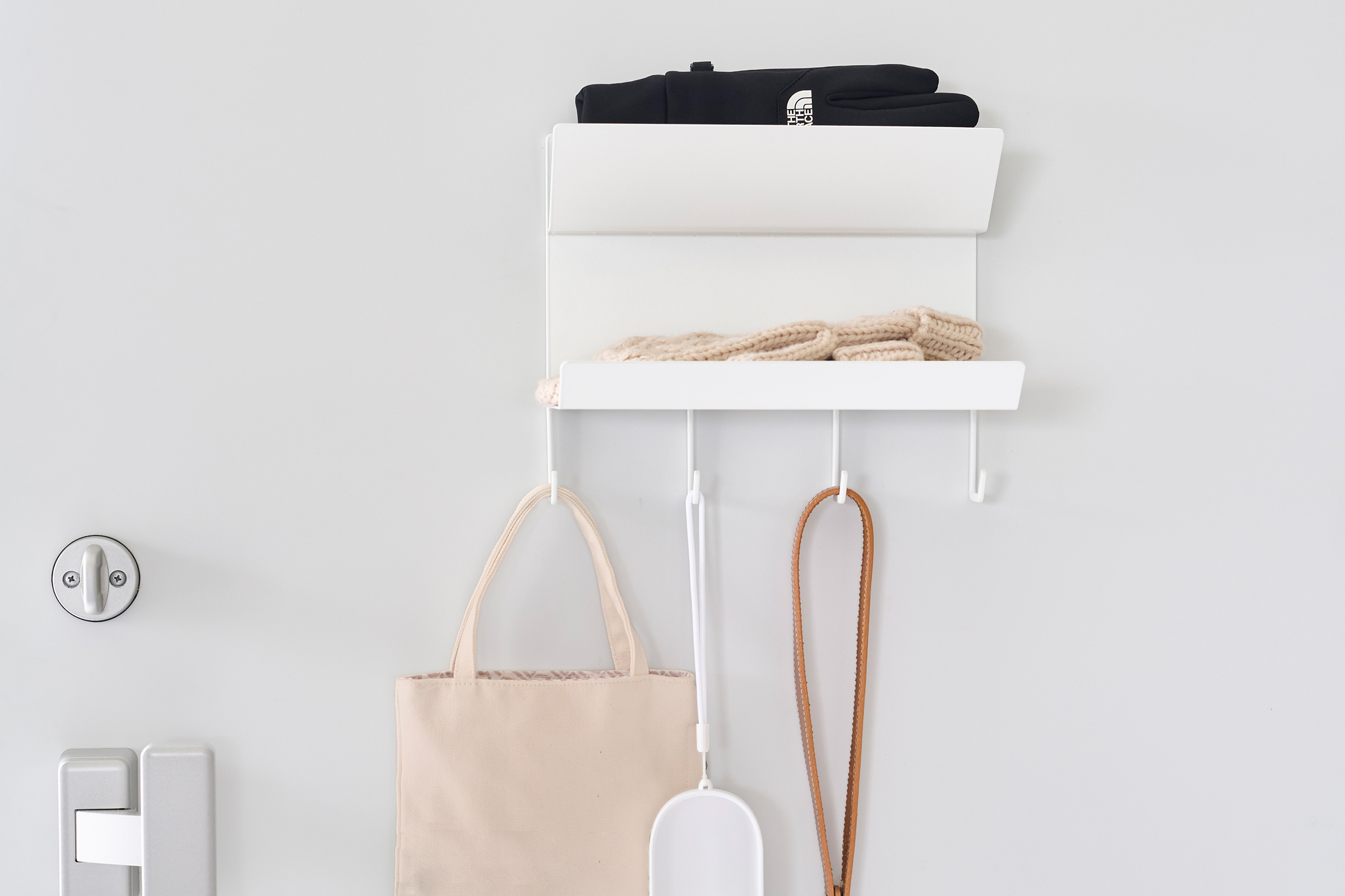 Front view of the Magnetic Entryway Rack by Yamazaki Home in white mounted on a door. Various entryway items are stored on the rack including gloves and a dog leash.