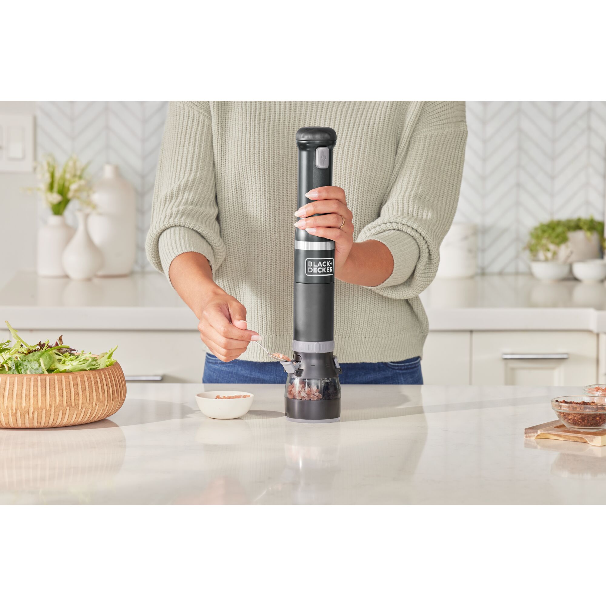 Talent adding salt crystals to the black, BLACK+DECKER kitchen wand spice grinder attachment