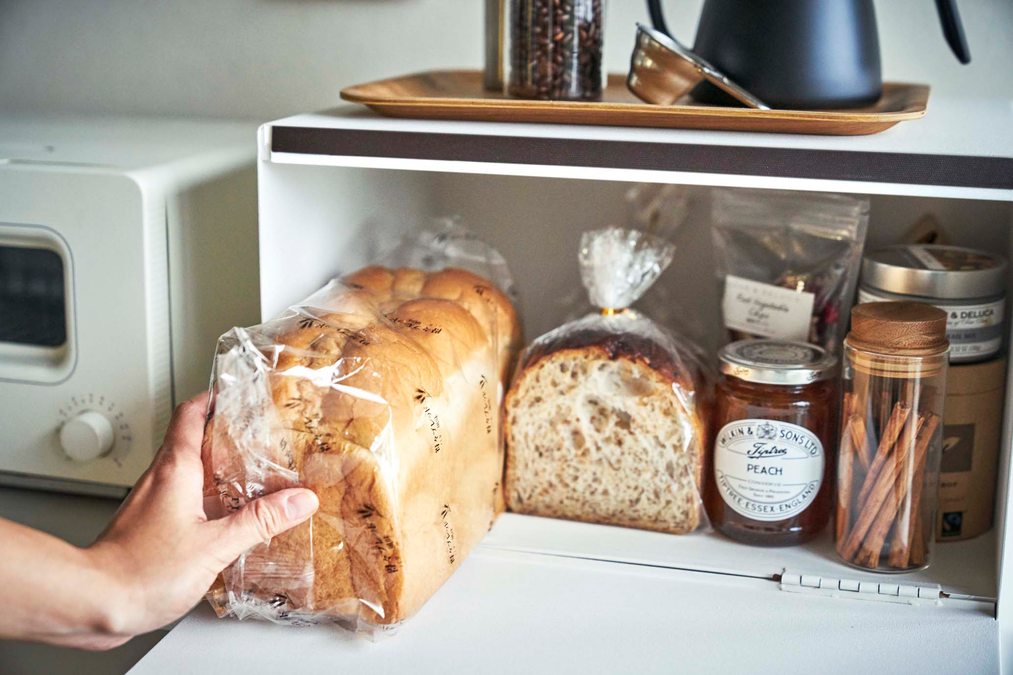 Front view of Yamazaki Home Bread Box holding bread loaves, jams, and spices. 