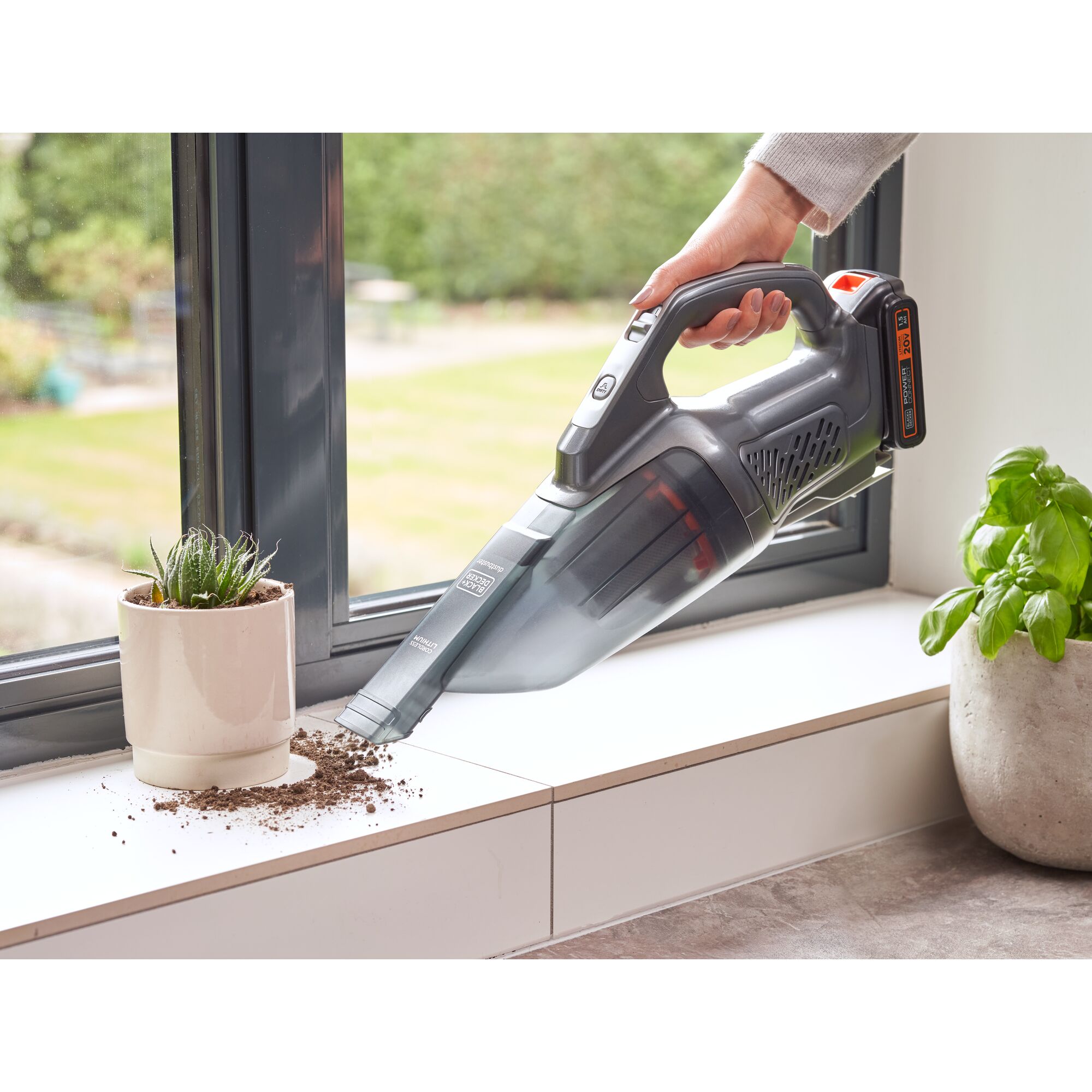 Person using 20 volt MAX Powerconnect handheld vacuum to clean up spilled dirt next to a potted plant on a window sill