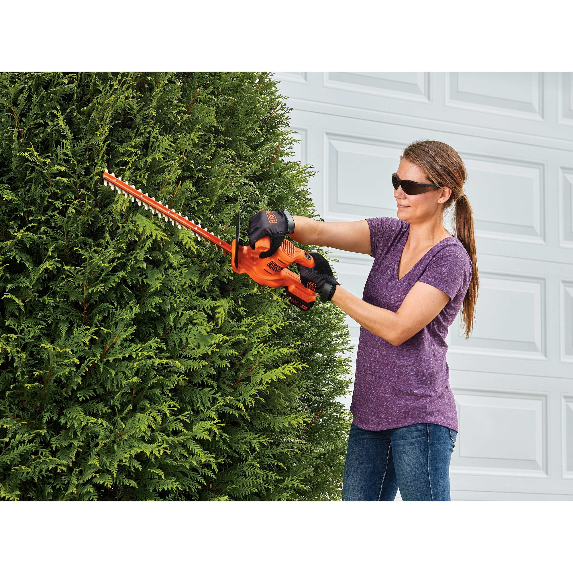 18 inch Cordless Hedge Trimmer being used by person to trim hedge outdoors.