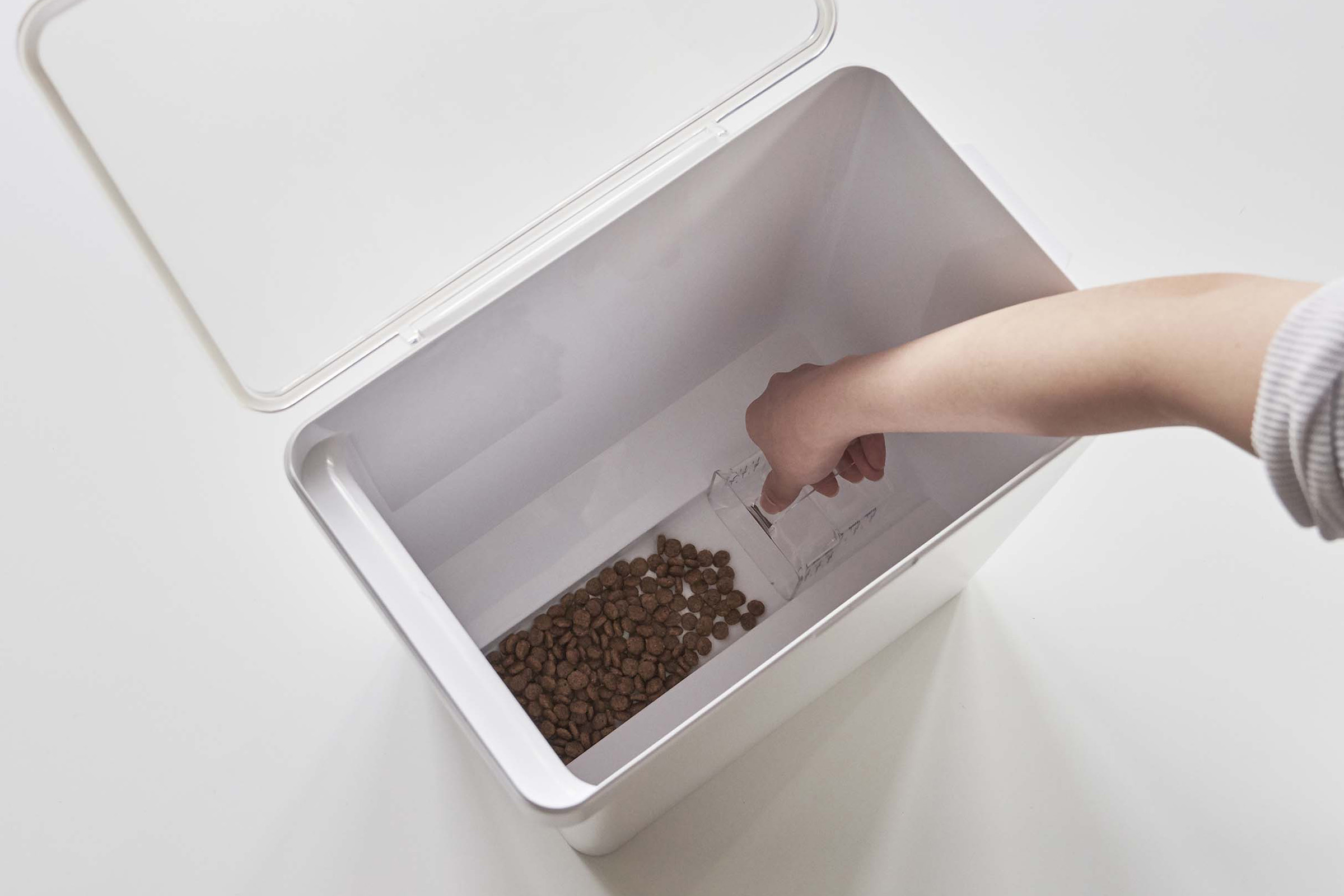 Aerial view of person scooping pet food out of white Airtight Food Storage Container on white background by Yamazaki Home.