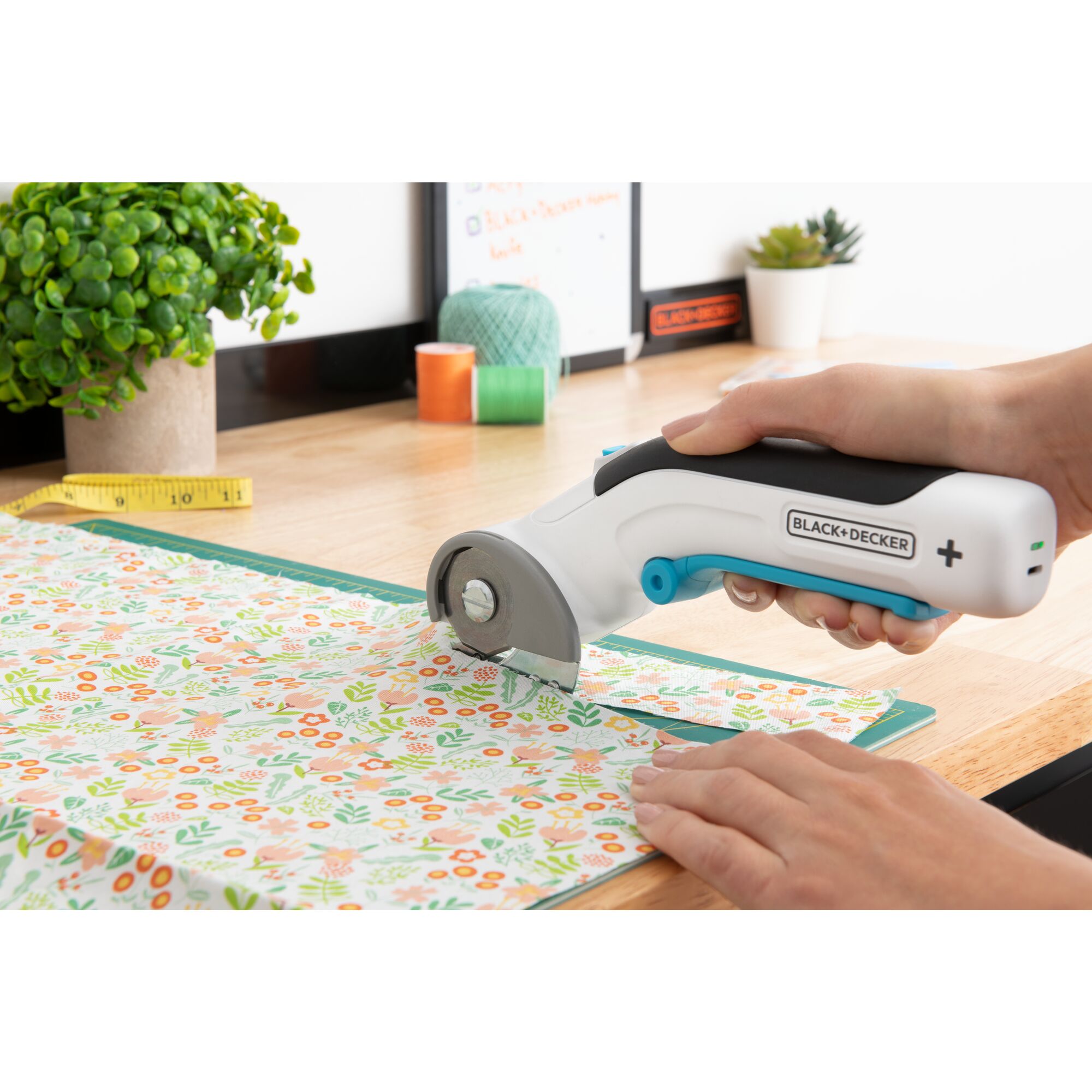close-up of a BLACK+DECKER power rotary cutter being used to cut floral fabric