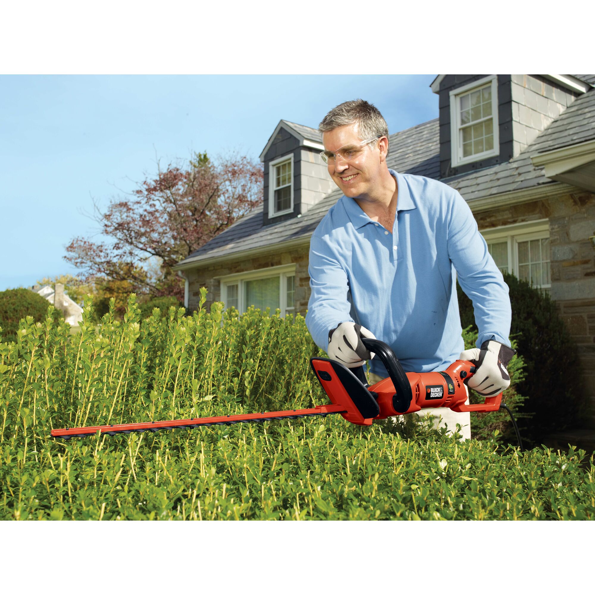 24 inch hedge trimmer with rotating handle being used by a person to trim a hedge.
