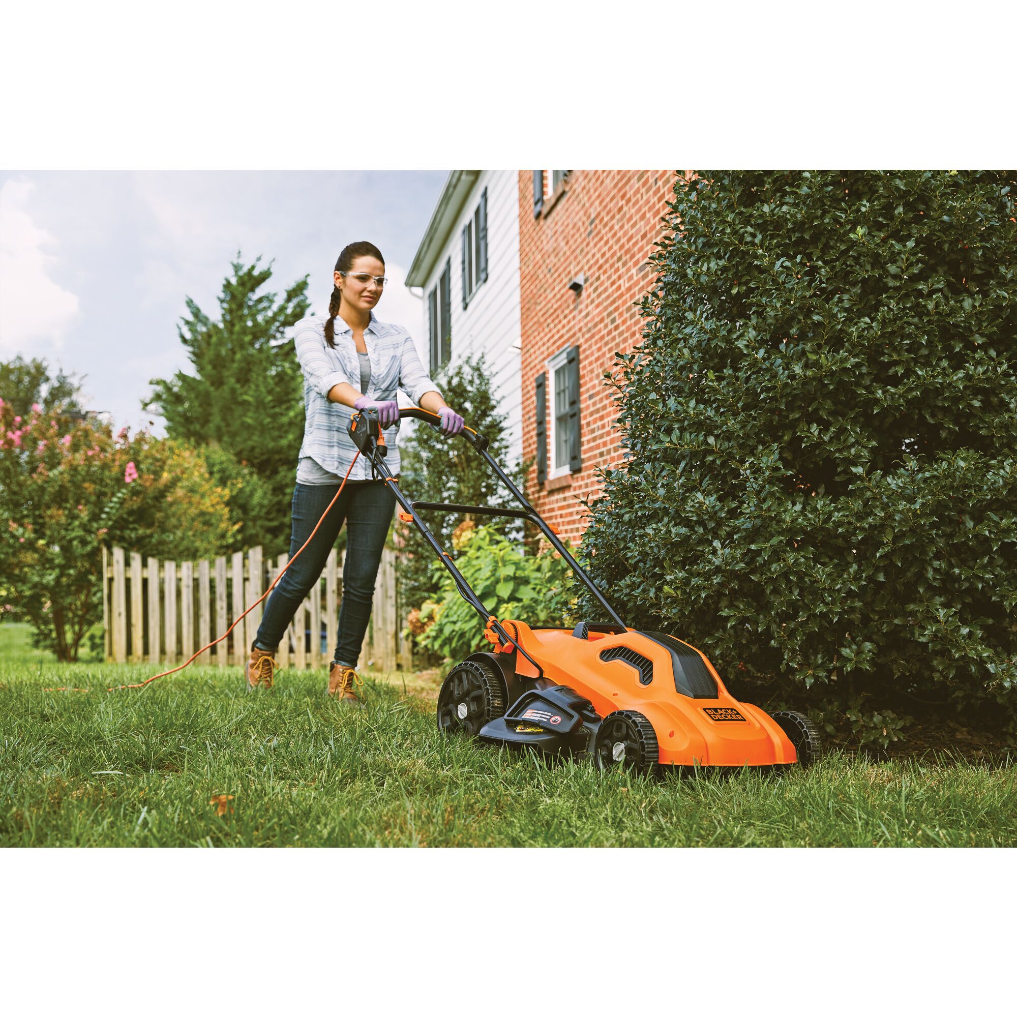 Corded electric lawn mower being used by a person to cut grass.