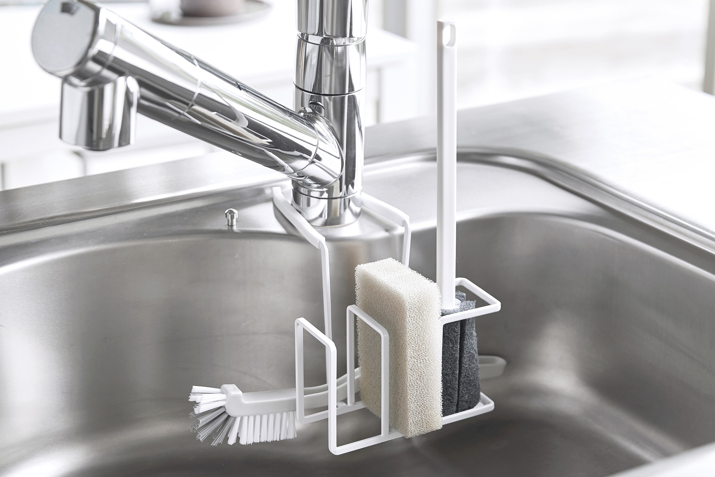 Faucet-Hanging Sponge & Brush Holder by Yamazaki Home in white holding several cleaning tools.