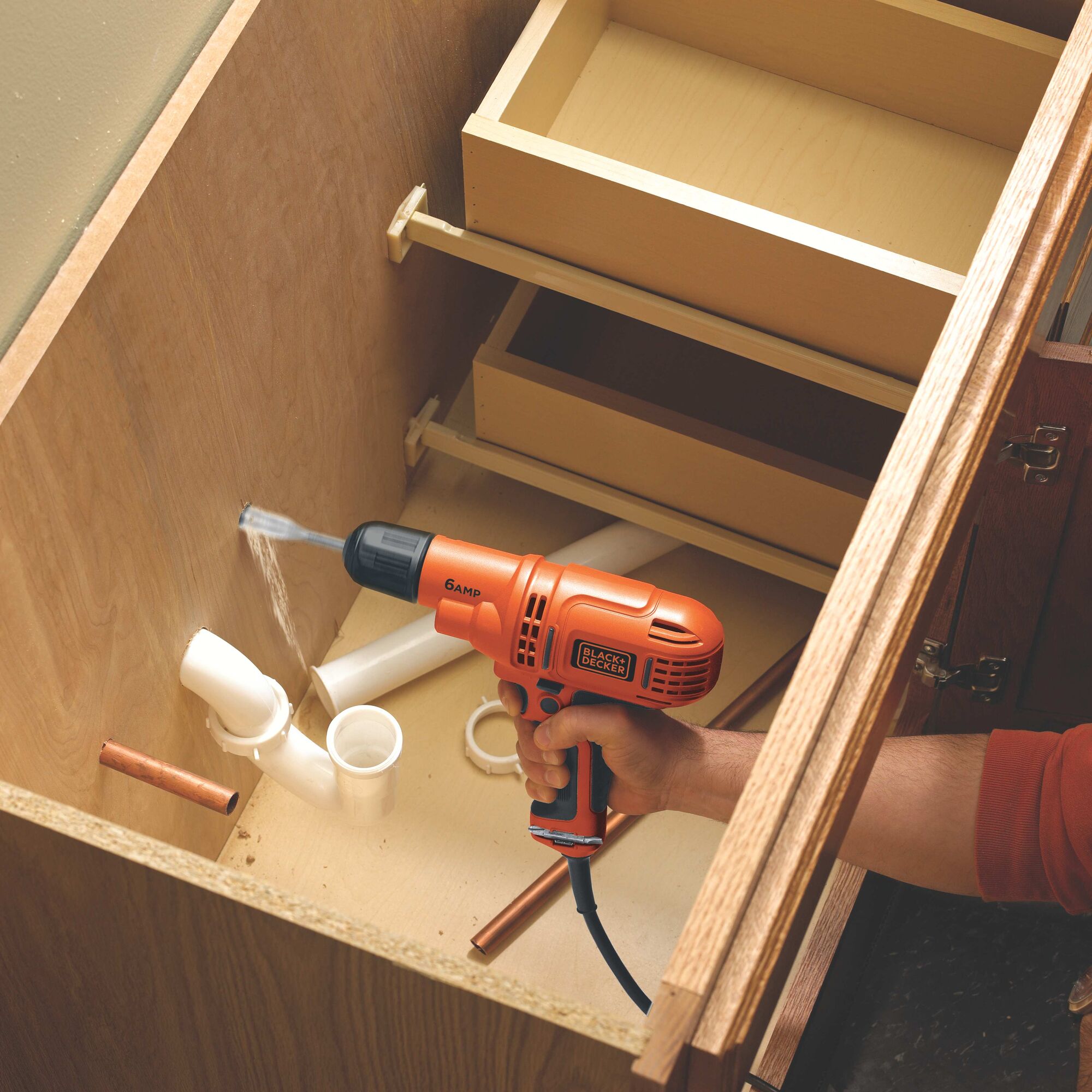 The Black and decker 6 amp 3 eighths inch drill driver being used by a person to drill a hole inside a wooden vanity