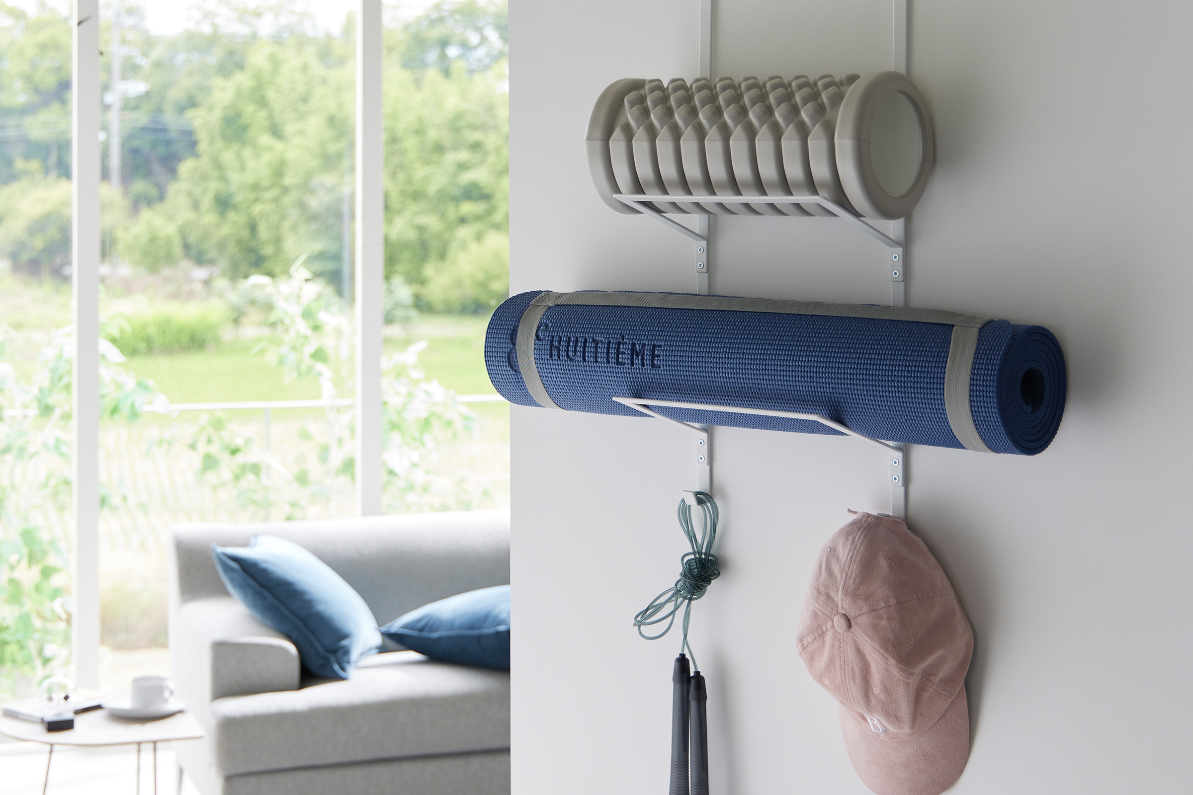 Over-the-Door Fitness Equipment Hanger by Yamazaki Home in white hanging on a door storing exercise mats and a hat.