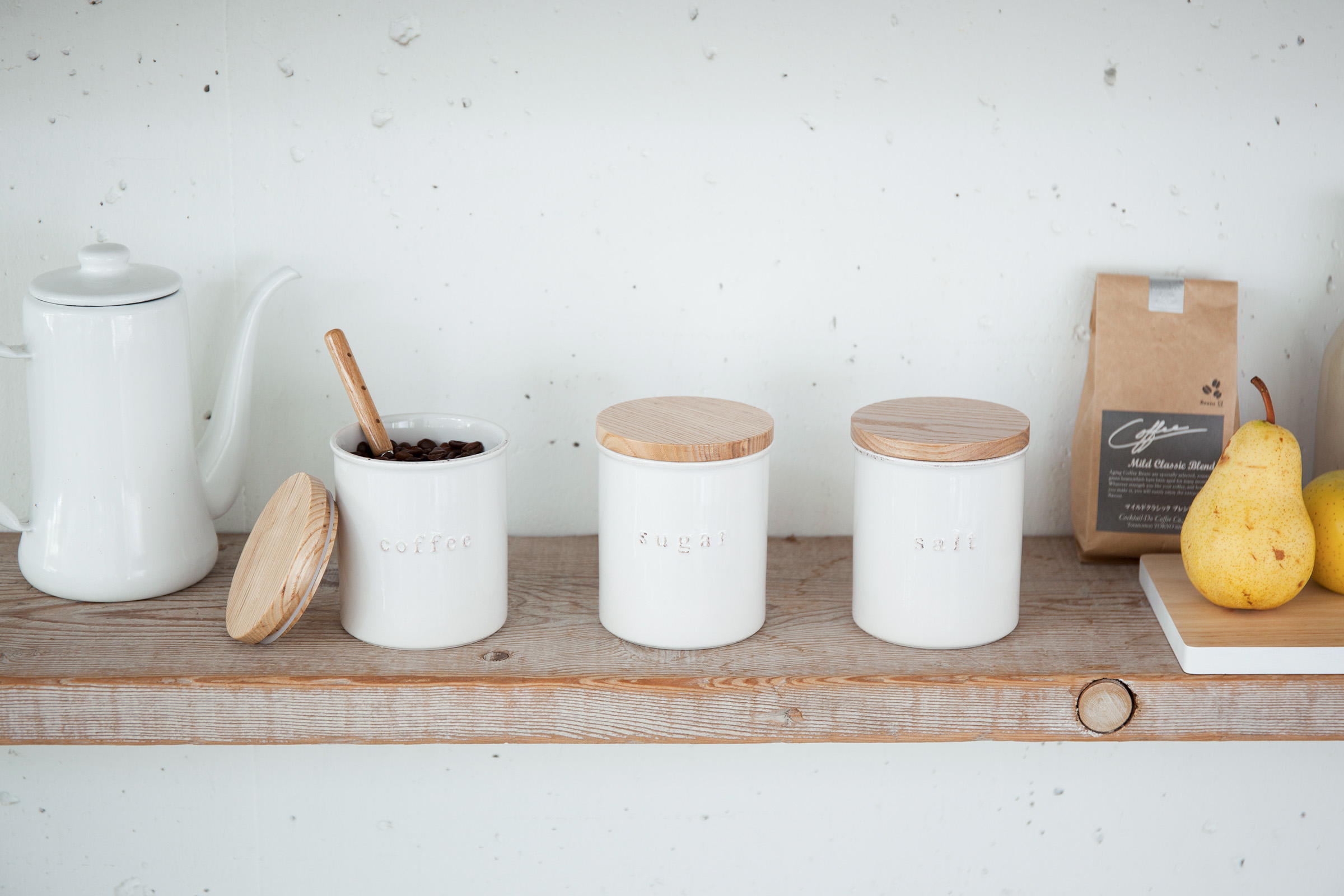 Wooden shelf with three white ceramic containers with wooden-lids.