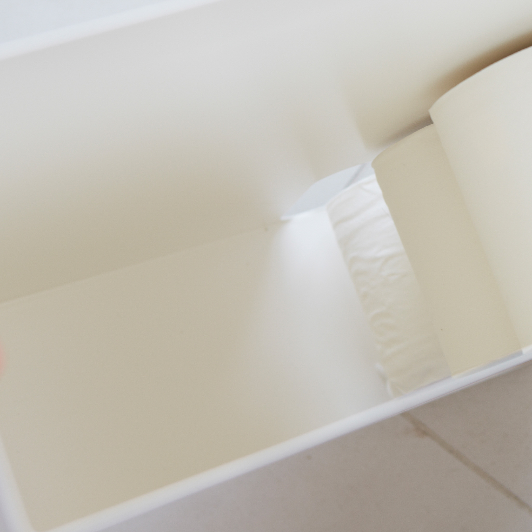 Vue de face d'un stockeur de papier toilette blanc Yamazaki Home contenant du papier toilette et des objets de d?coration dans une salle de bain.