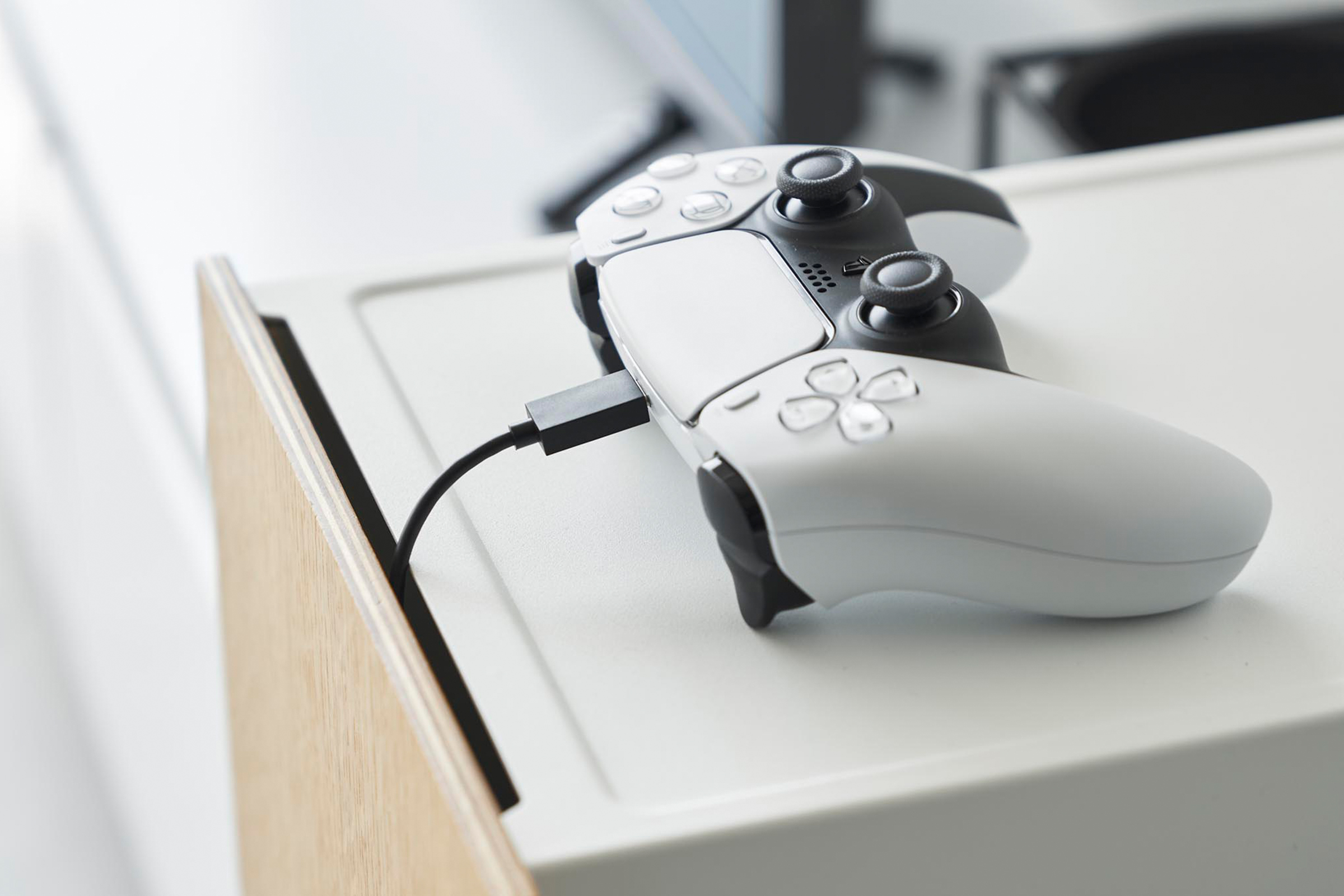 A game controller is placed on the white video game storage cabinet. A slit between the door and the cabinet allows the controller's cable to come through from the inside of the cabinet.