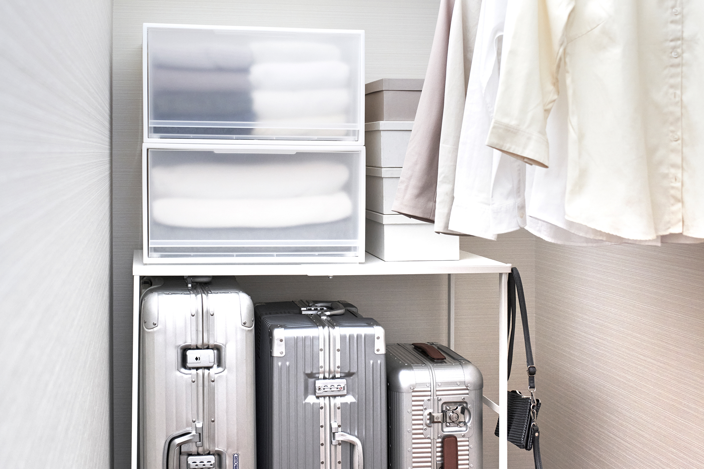 Close up of white Yamazaki Home Expandable Suitcase Rack in a closet with three suitcases underneath