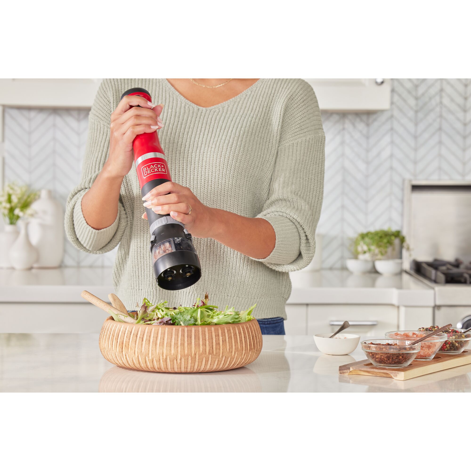 Talent using the red BLACK+DECKER kitchen wand spice grinder attachment to add spices to a salad