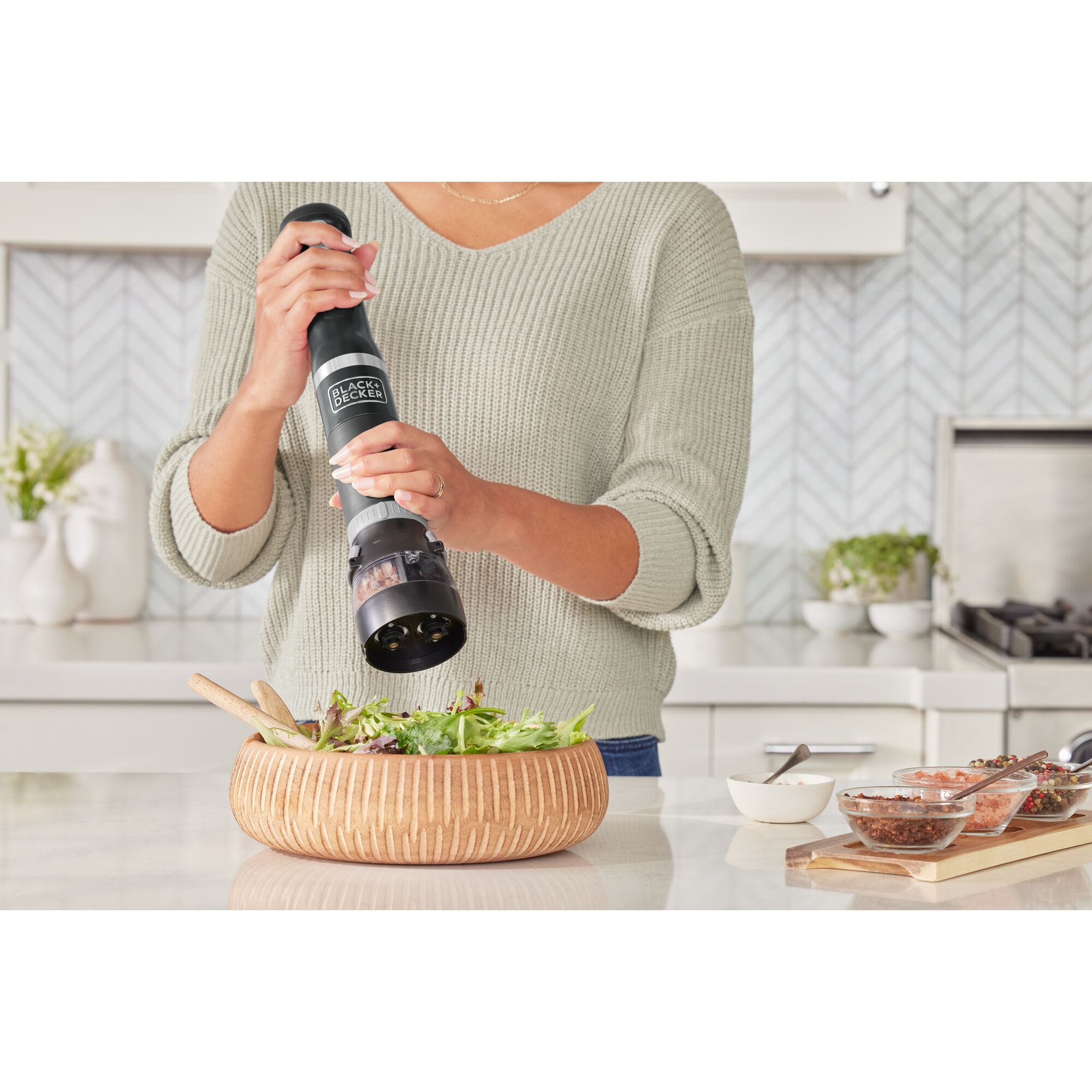 Talent using the black BLACK+DECKER kitchen wand spice grinder attachment to add spices to a salad