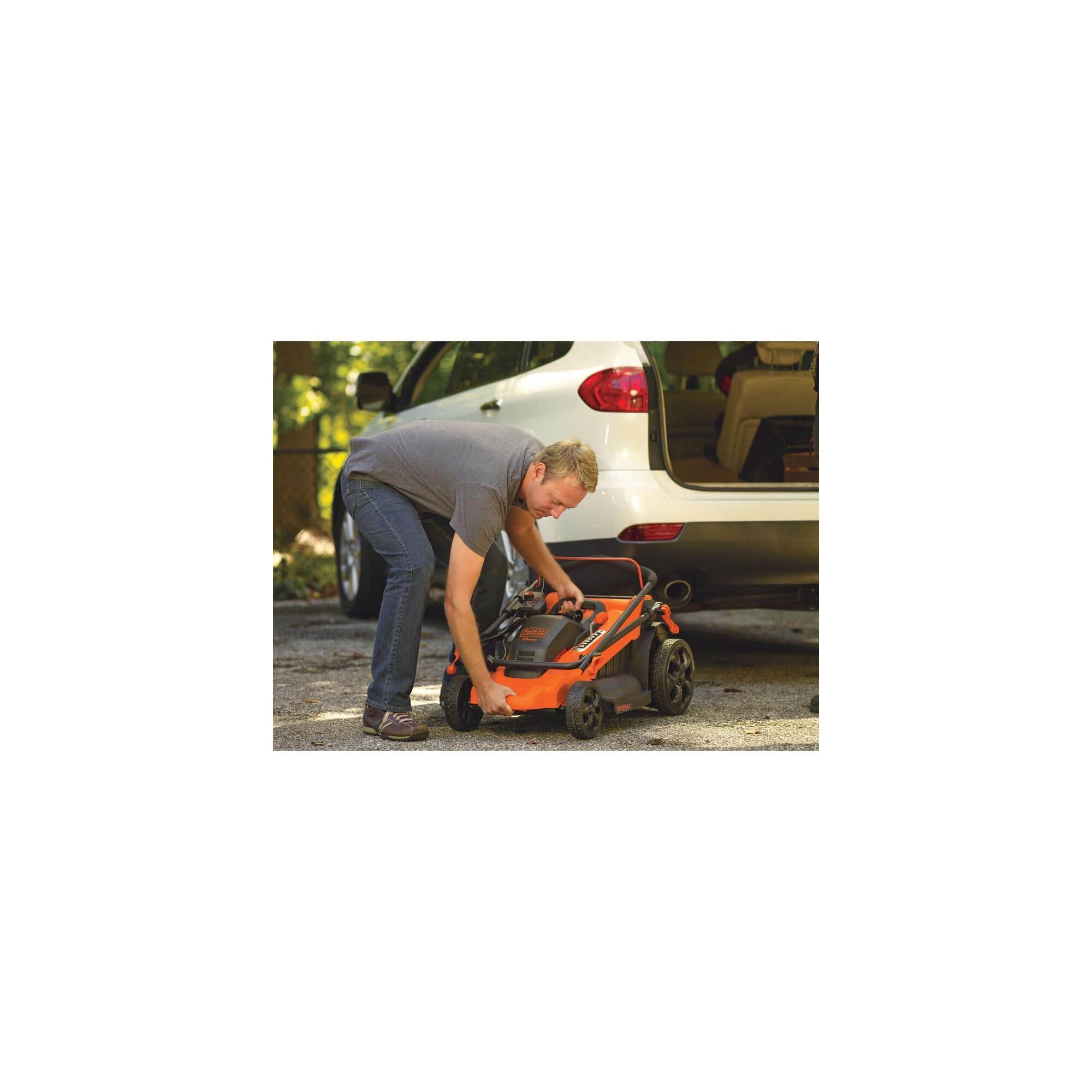 Person lifting portable lawn mower into the truck of a car