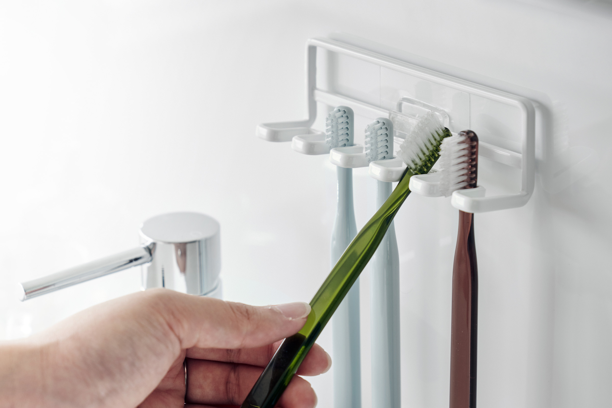 Yamazaki Home's Traceless Adhesive Toothbrush Holder, white, mounted on a bathroom wall with four colorful toothbrushes and a chrome faucet.