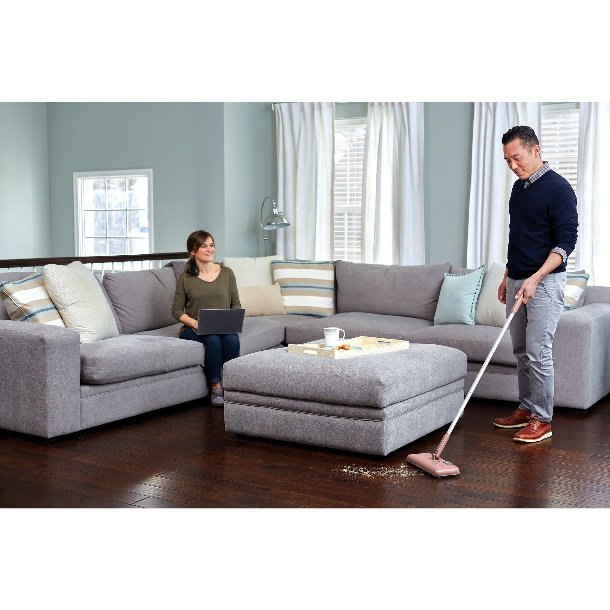 Powered Floor Sweeper being used by person to clean messy floor in sitting area of house.
