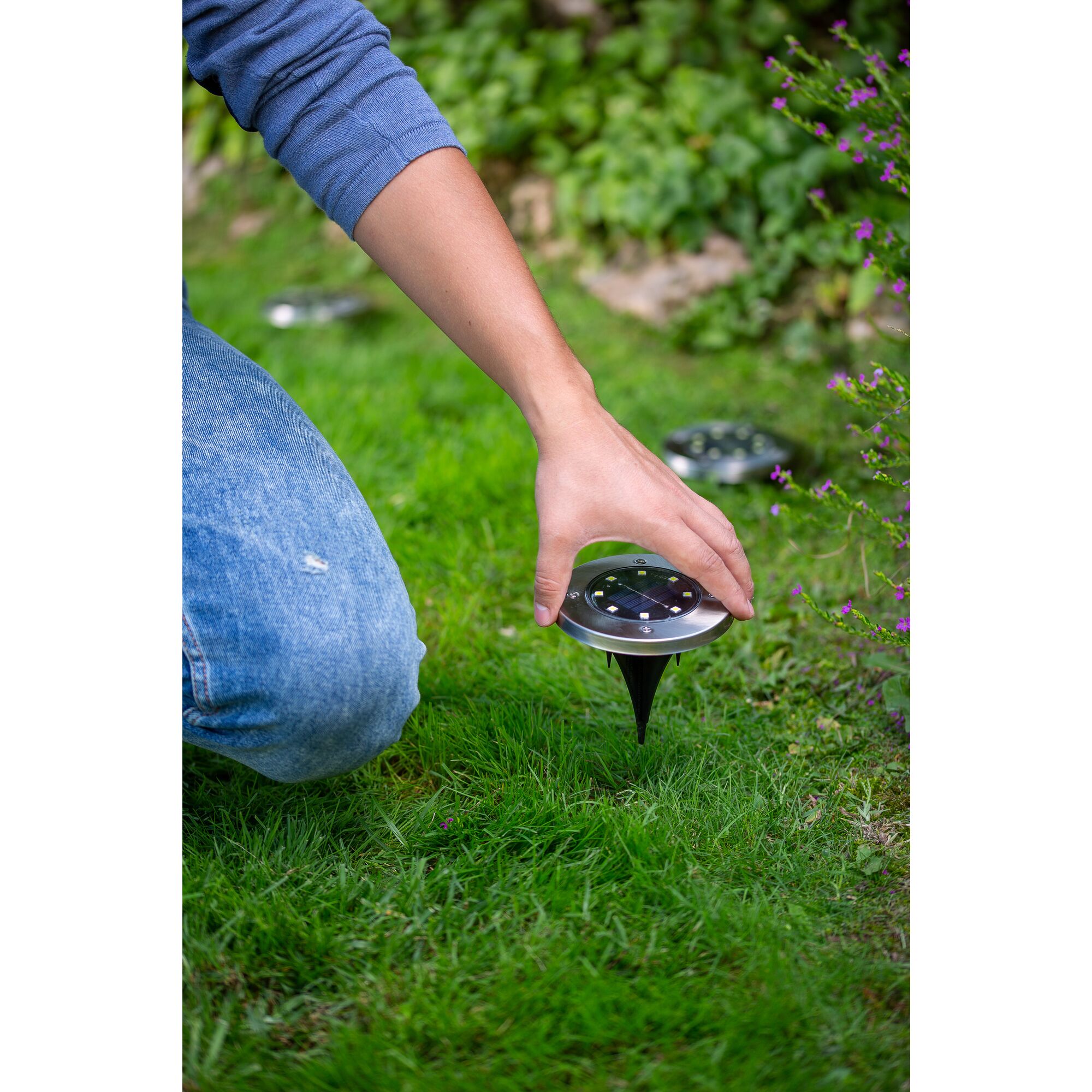 Hand pushing the BLACK+DECKER Solar Disk Light into the ground.