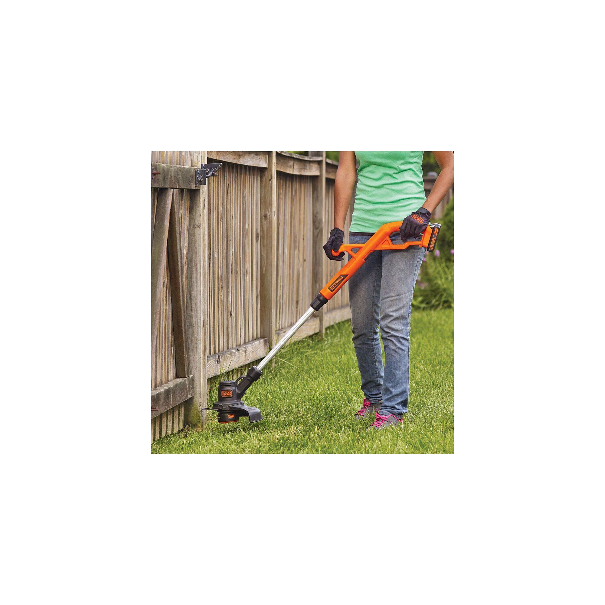 Person using string trimmer near wooden fence
