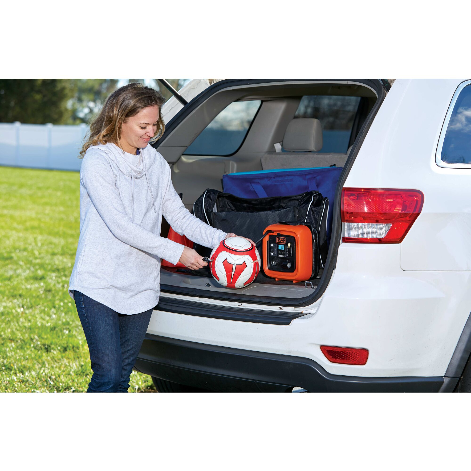 12 volt D C Multi Purpose Inflator placed in the back seat of S U V being used by person to inflate soccer ball.
