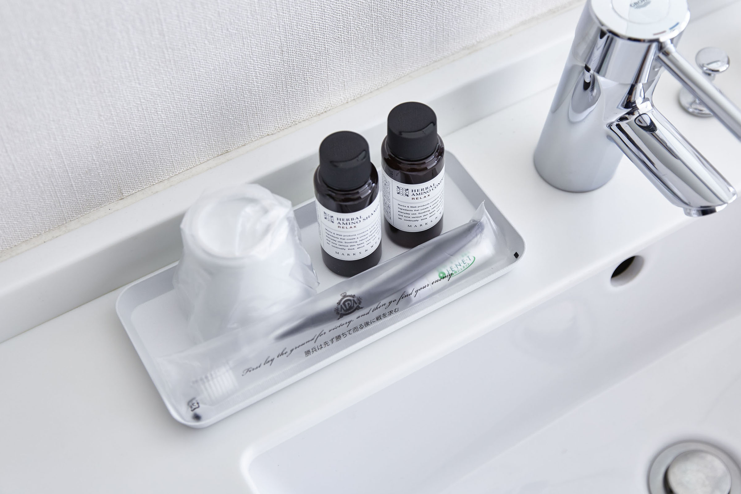 White Amenity Tray | Rectangular holding a toothbrush, a cup and shampoo bottles next to a faucet on white sink