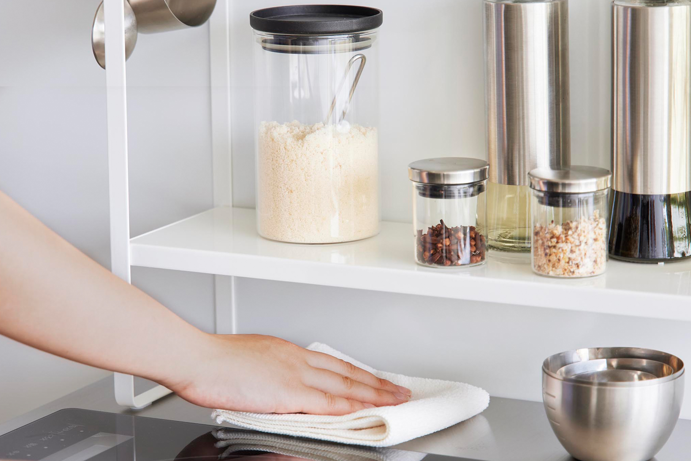 Close-up image of the Two-Tier Countertop Rack by Yamazaki Home in white. A hand is shown wiping the space underneath.