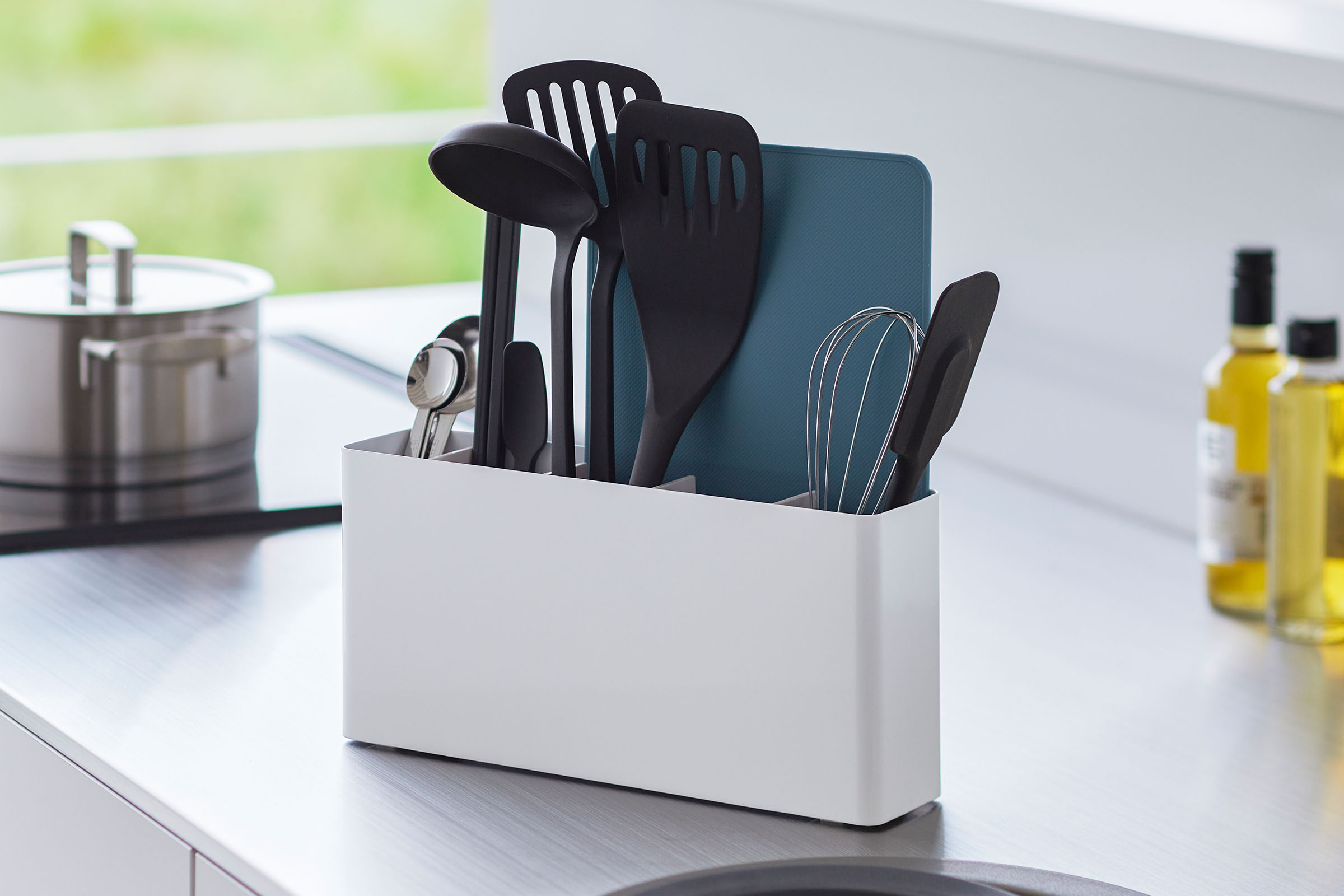 White Utensil & Thin Cutting Board Holder by Yamazaki Home on a kitchen counter, holding various utensils and a cutting board.