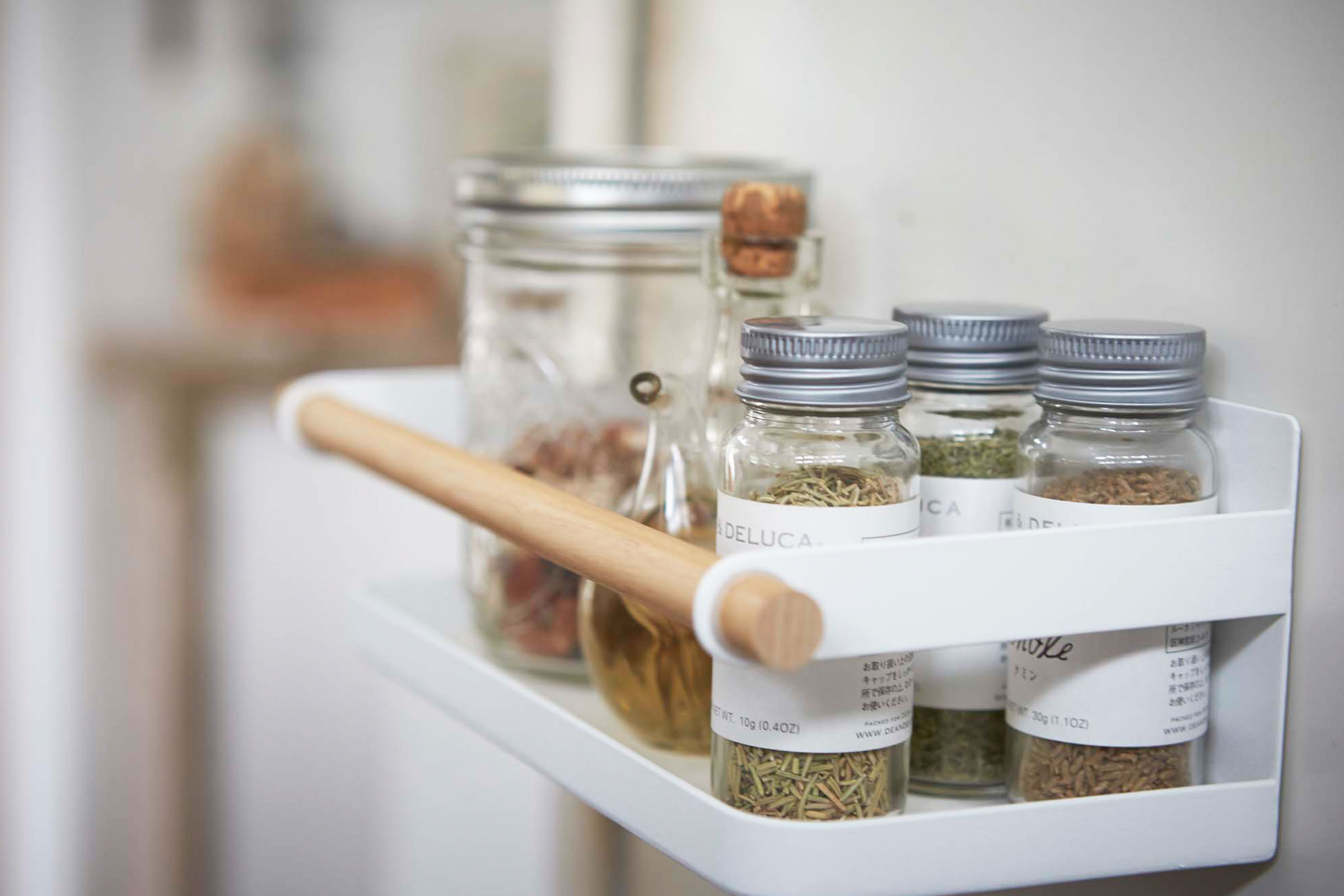 Close up side view of white Wall-Mounted Storage Caddy holding spices in kitchen by Yamazaki Home.