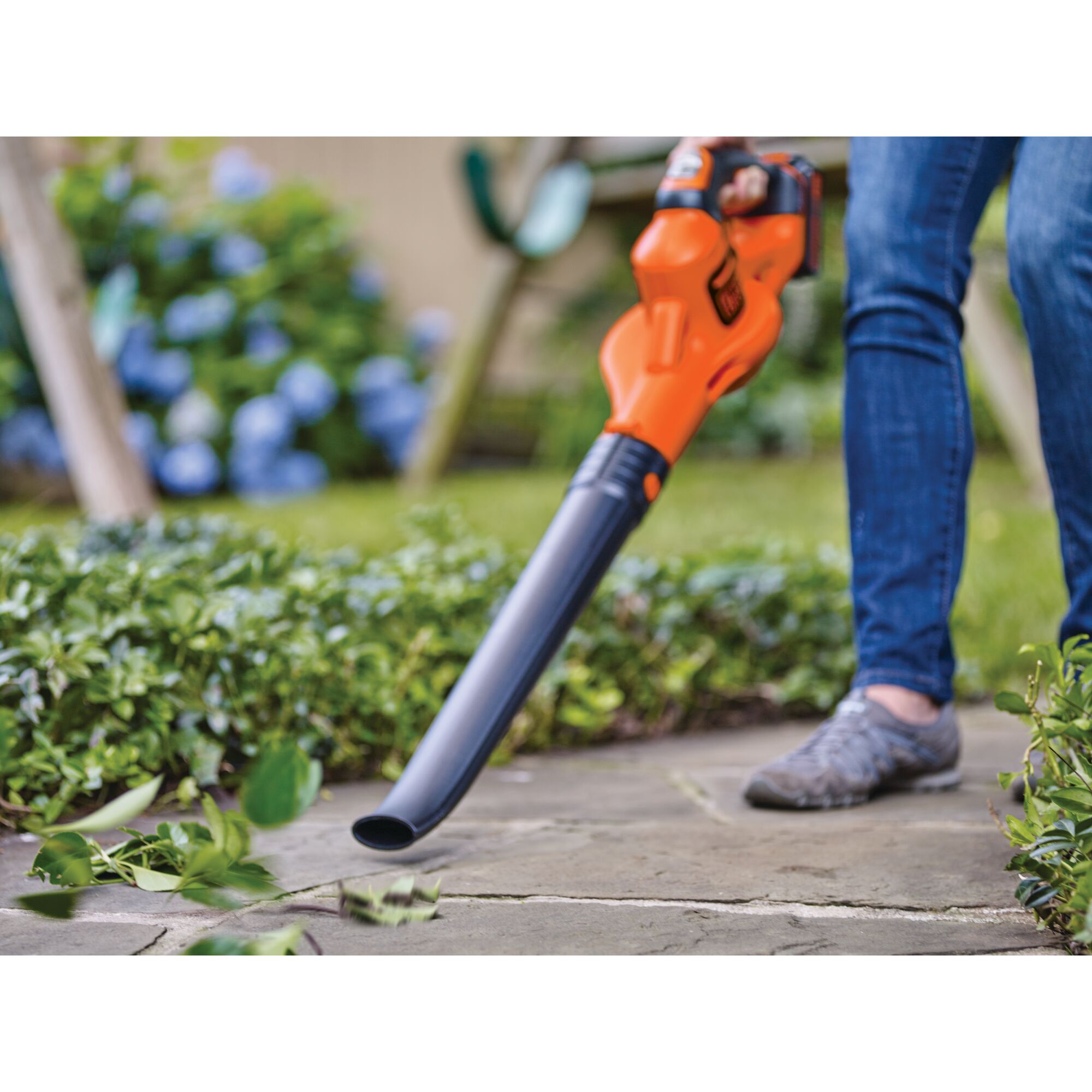 Close-up of someone using 20V Max Lithium Powerboost Sweeper to clear leaves from a walkway.