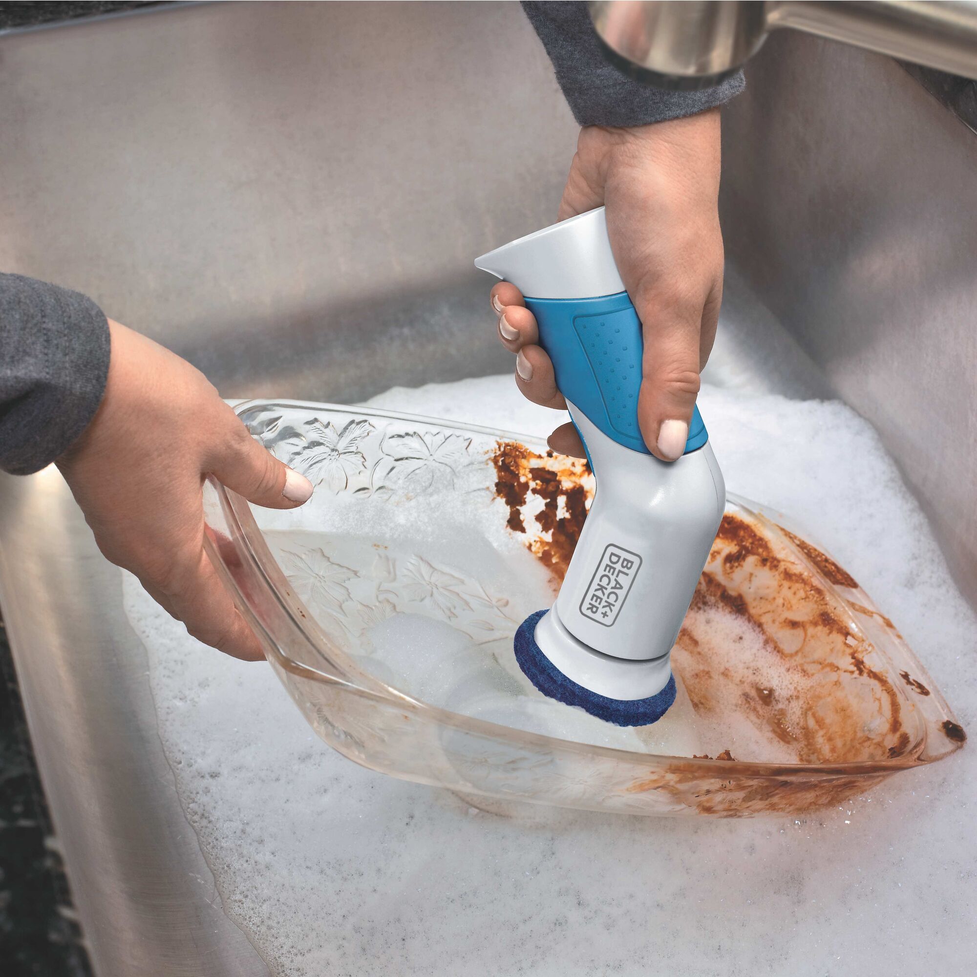Woman using Power Scrubber Brush to clean a dirty dish in a sink.