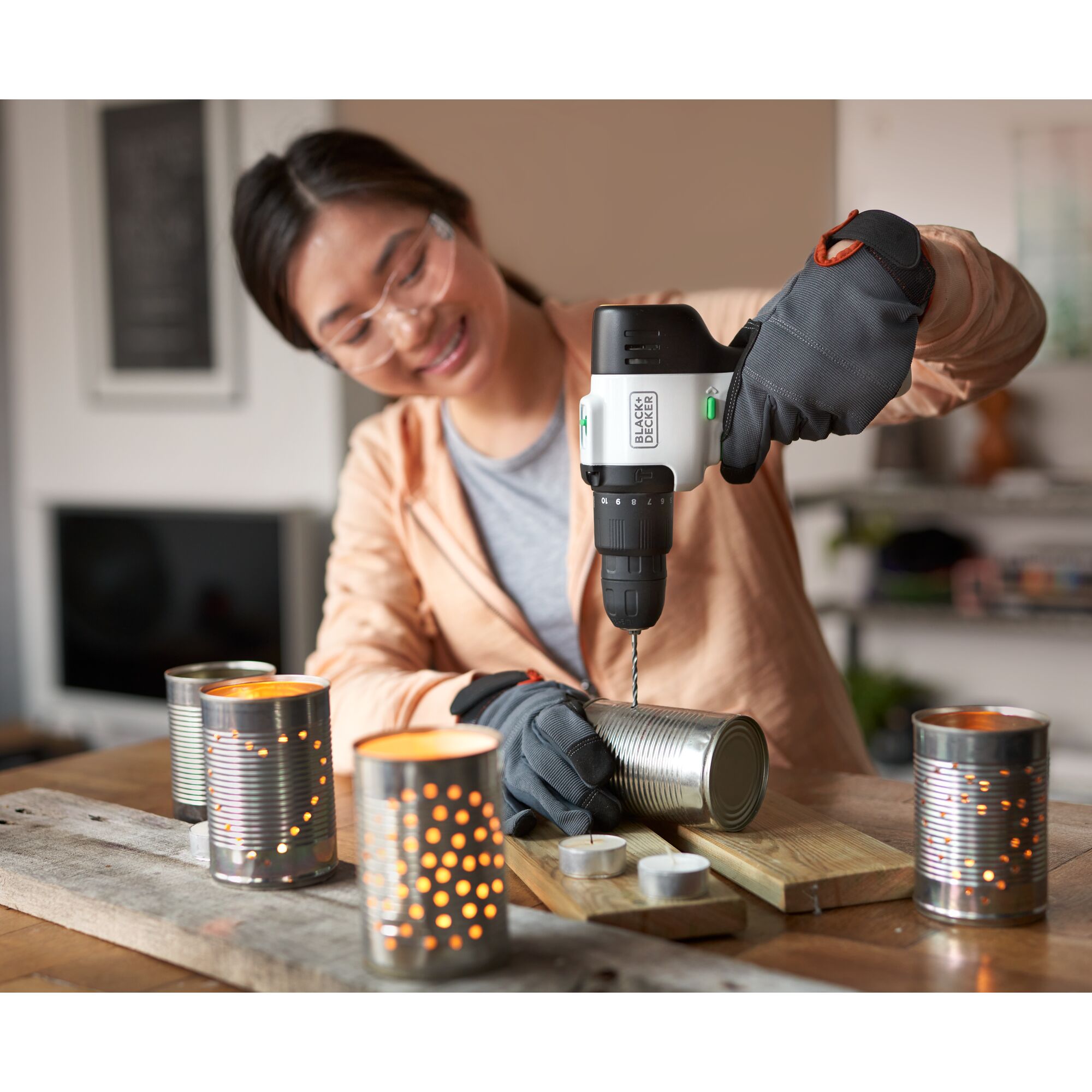 Woman using reviva™ 12V MAX* Hammer Drill/Driver to drill holes in soup cans for a craft project.