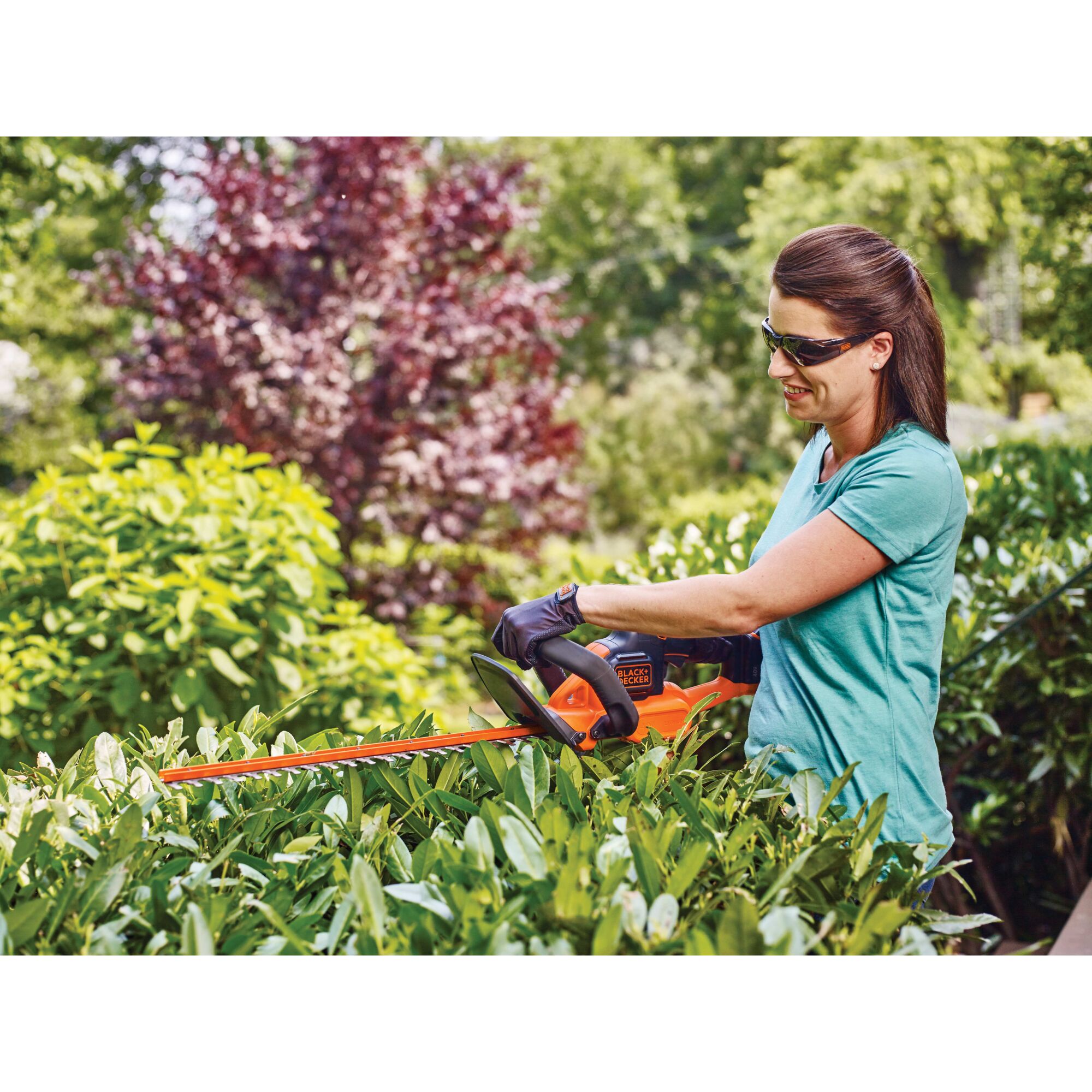 Woman using 40 volt Max 24 Inch Powercut Hedge Trimmer on top of bush.