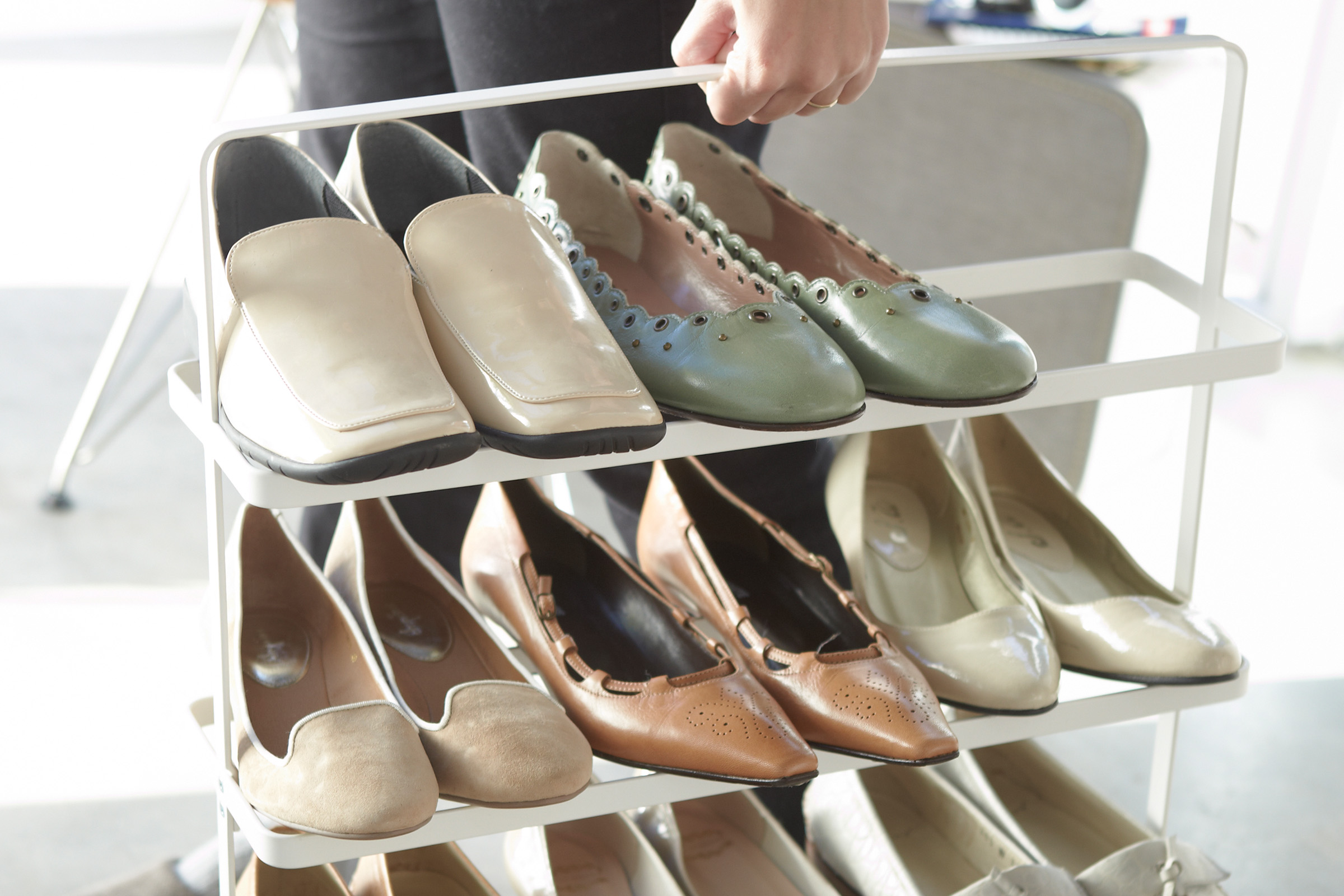 A hand lifting the Shoe Rack by Yamazaki Home in white containing multiple pairs of shoes.