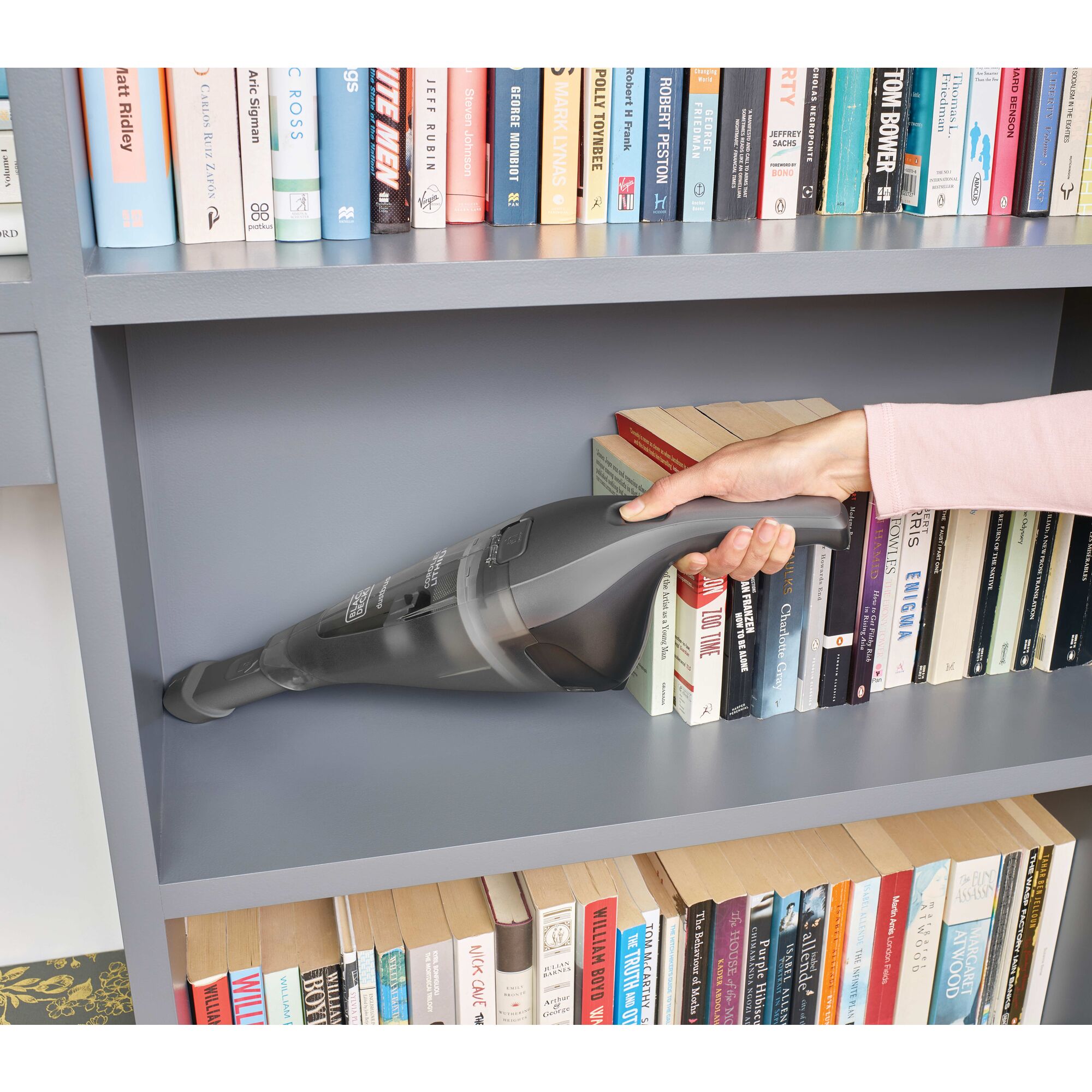 Person cleaning bookshelf with dustbuster handheld vacuum
