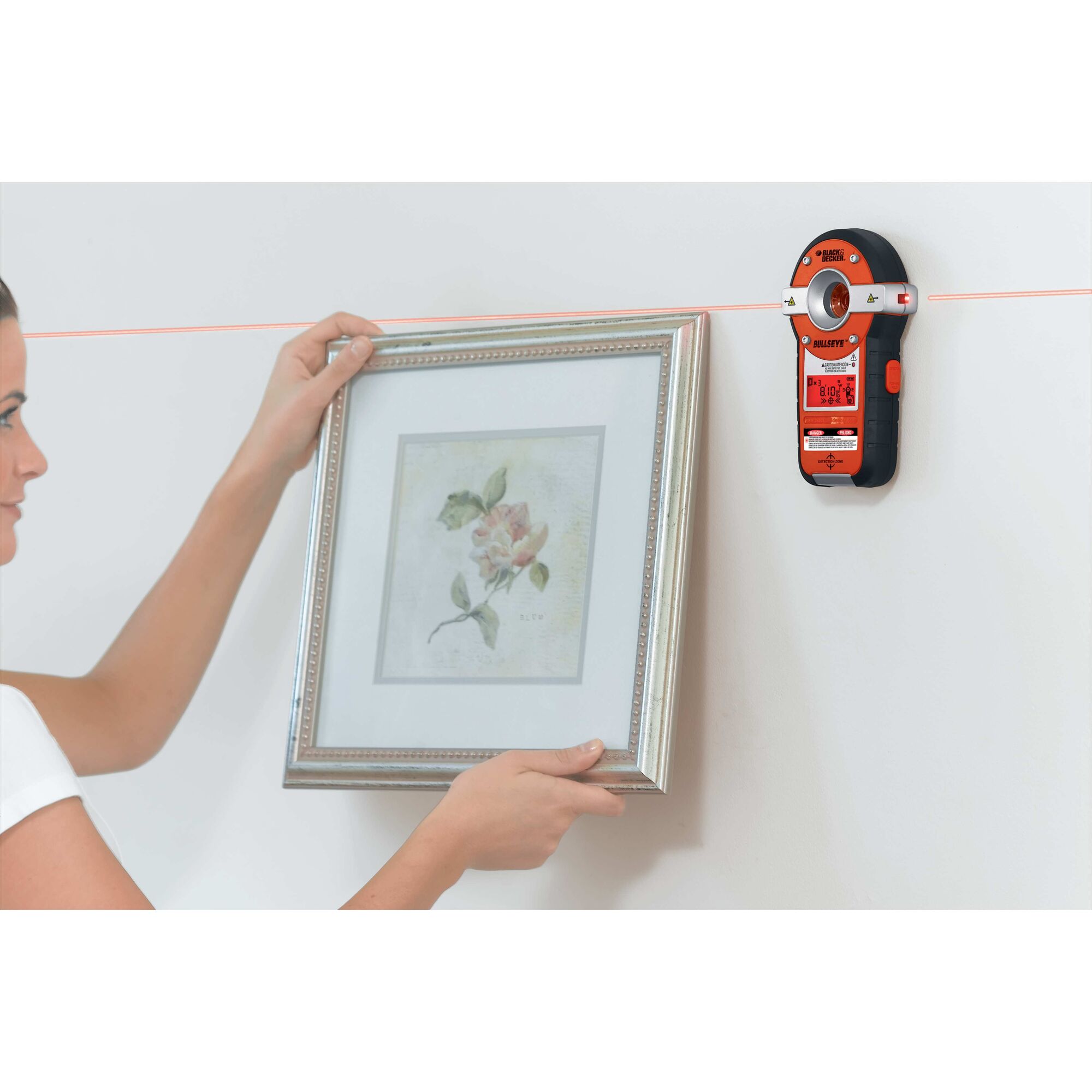 BullsEye Auto Leveling Laser with Stud Sensor being used by person to hang picture frame on wall.