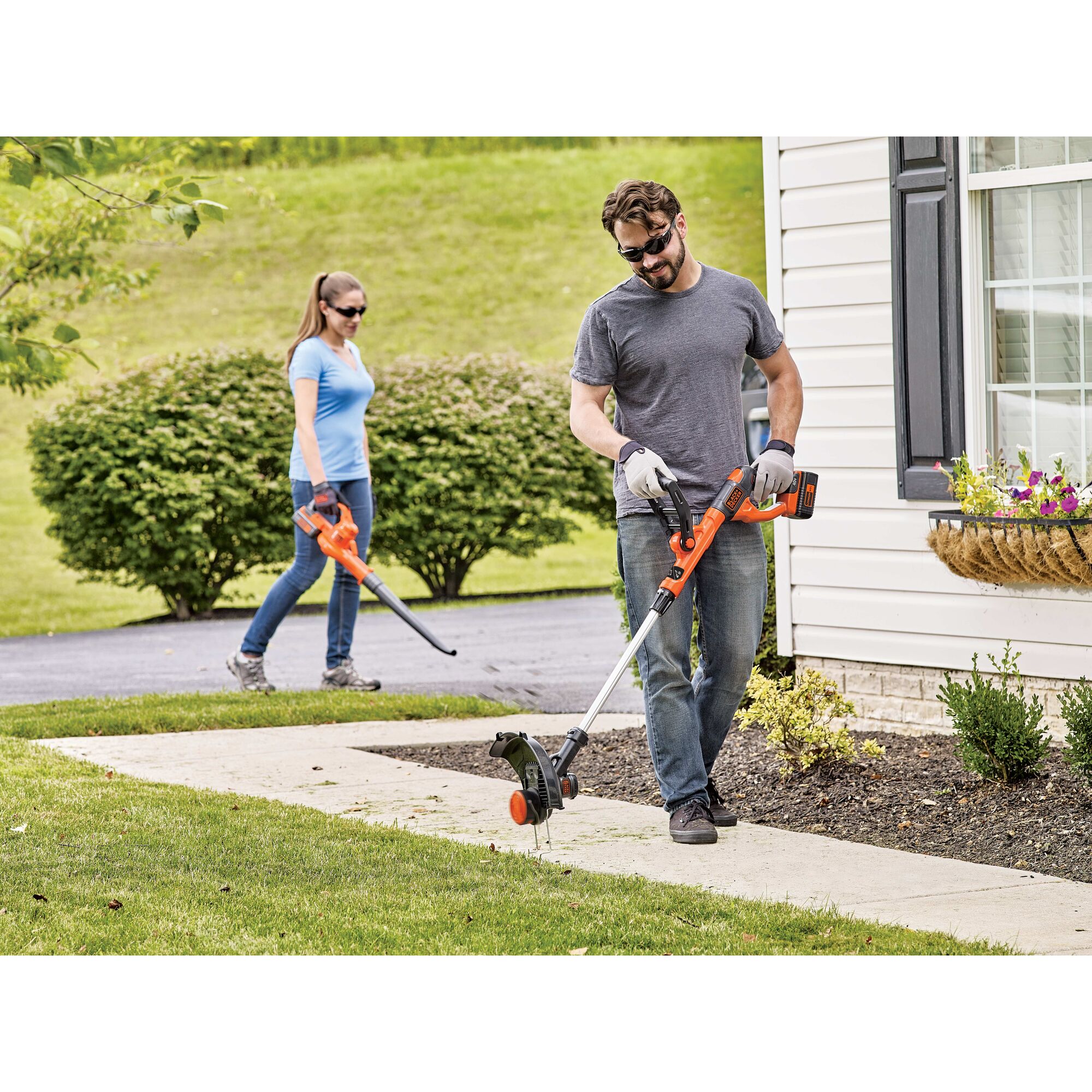 Couple doing yard word, one using string trimmer and other using leaf blower