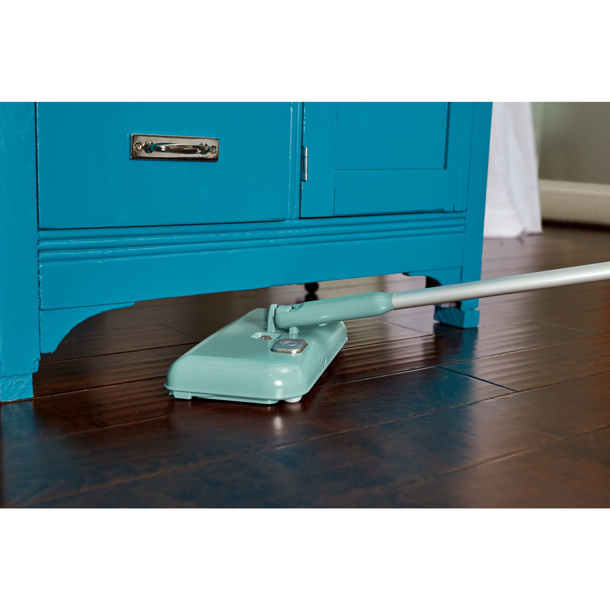 Powered classic mint floor sweeper being used to clean fllor underneath a  cabinet.