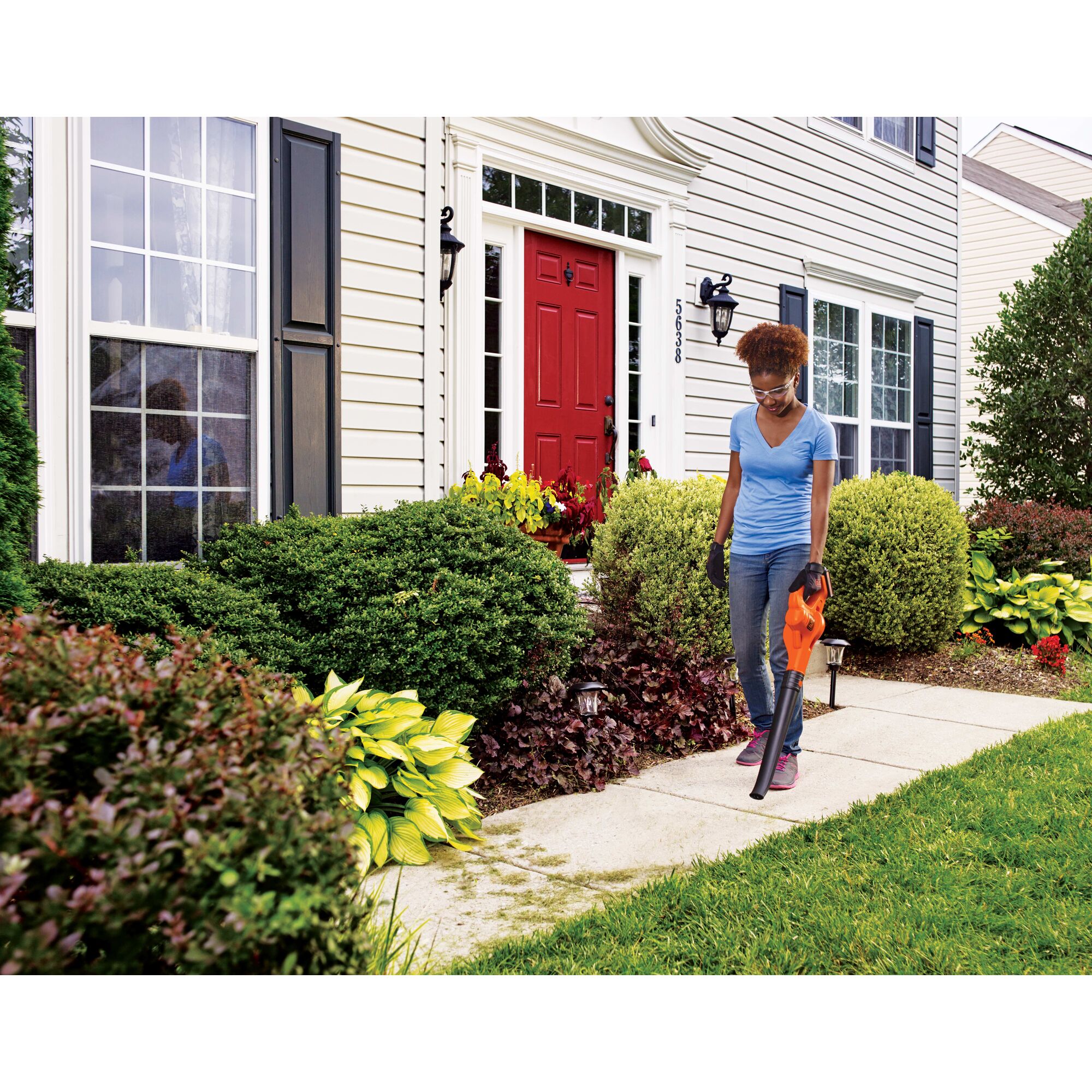 Woman using a 20V Max Lithium Sweeper on front walkway of a house.