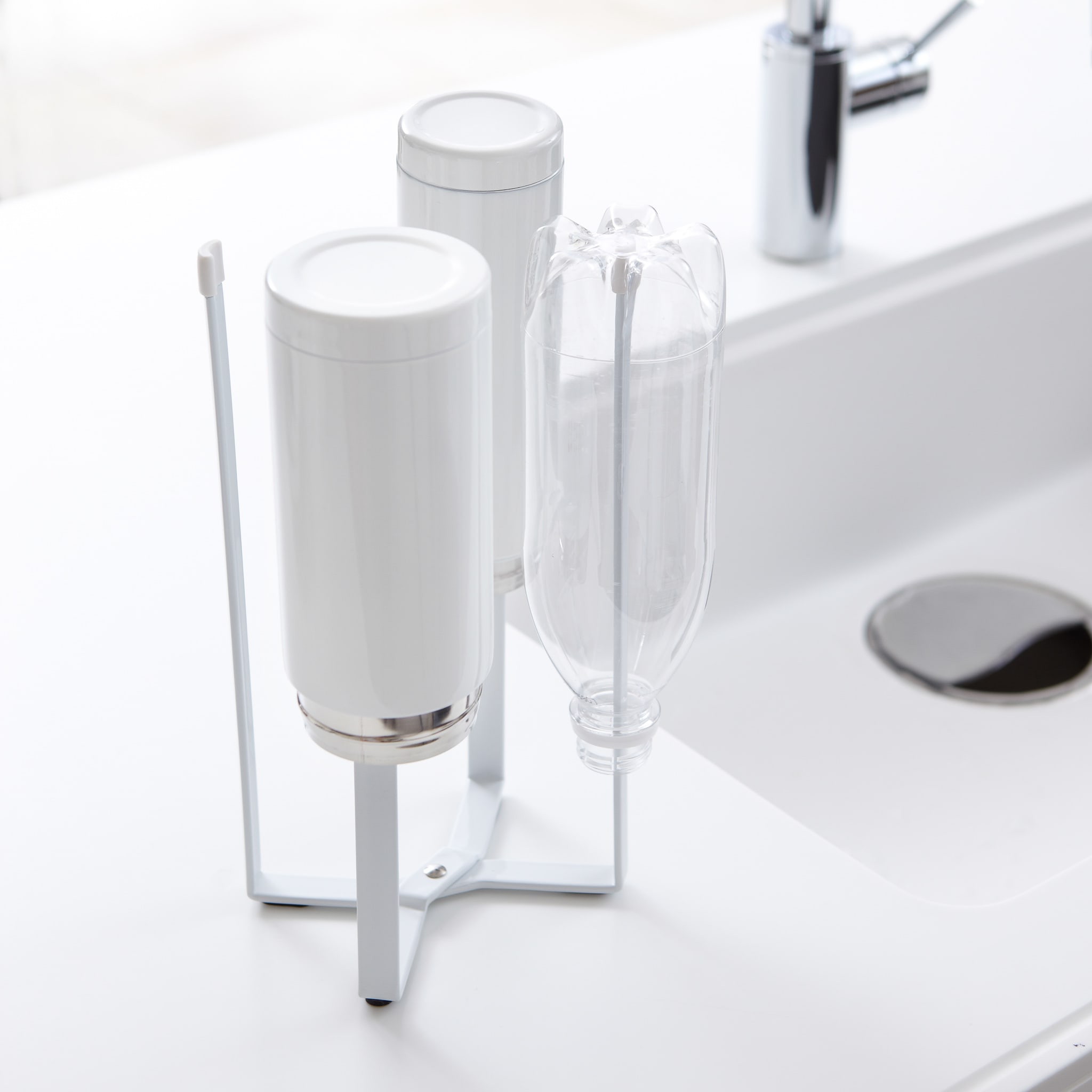 Vorderansicht des weißen zusammenklappbaren Flaschentrockners von Yamazaki Home zum Trocknen von Flaschen auf der Arbeitsplatte der Küchenspüle.