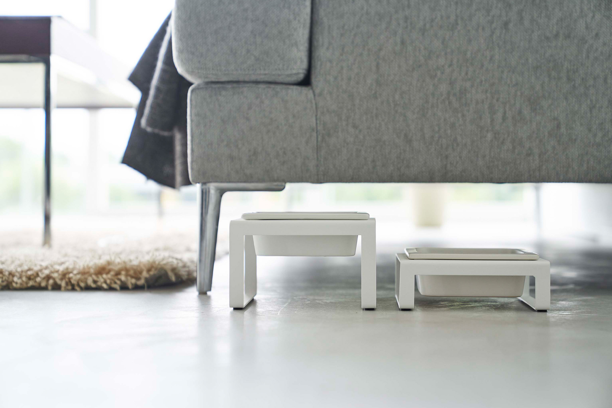 Side view of tall and short Single Pet Food Bowl by Yamazaki Home in white near a living room couch.