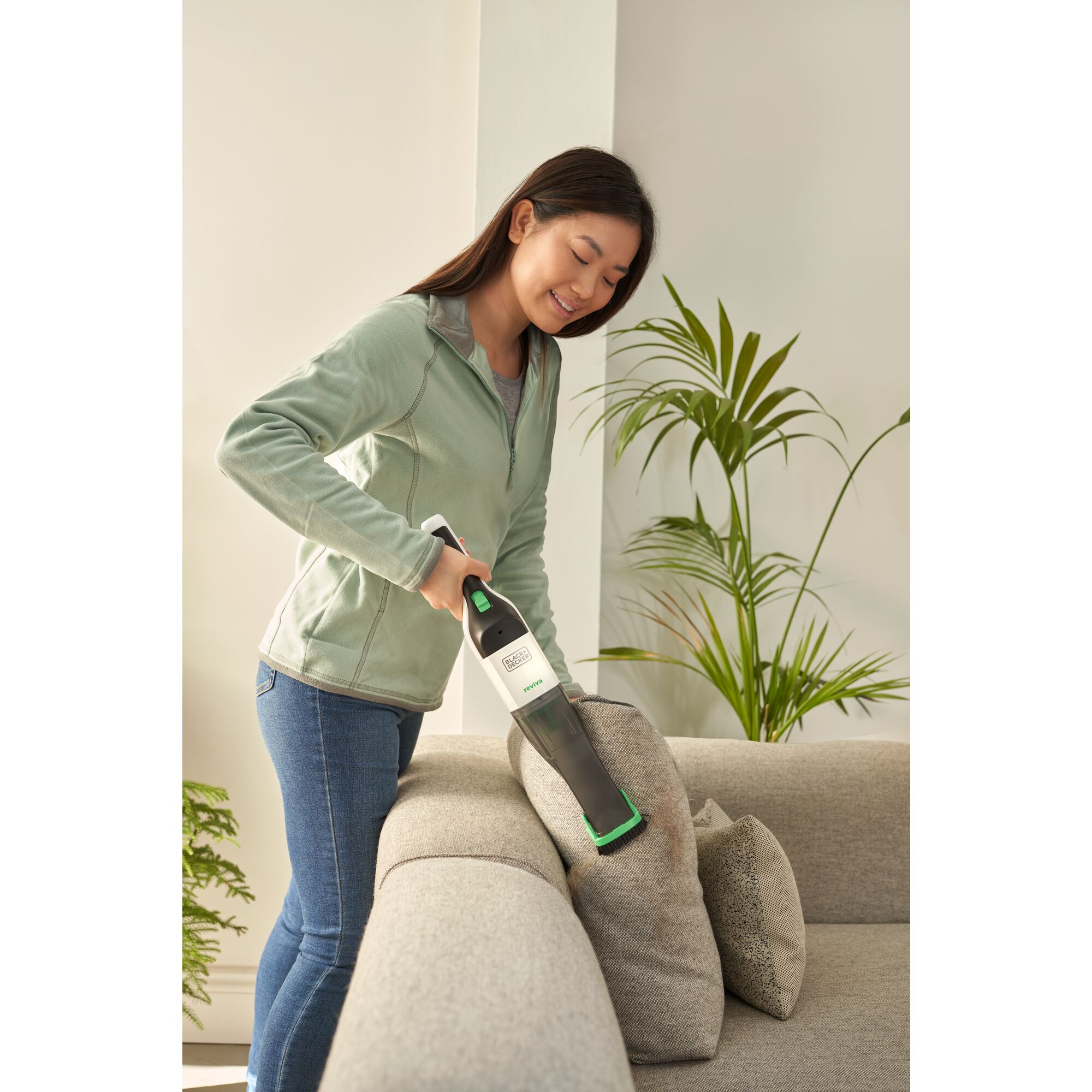 Woman cleaning sofa with the BLACK+DECKER reviva hand vac